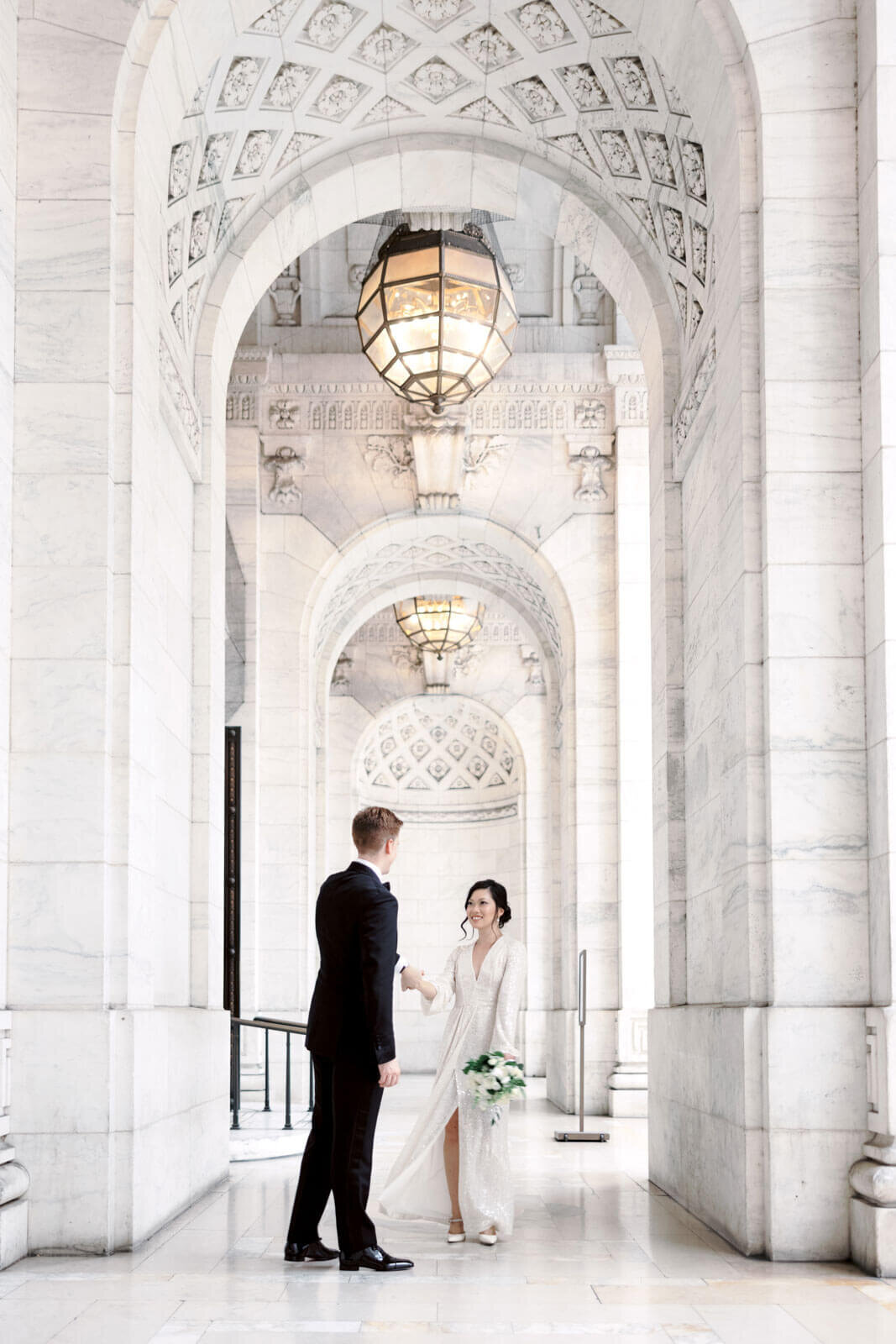 The bride is happily gazing at her groom while dancing in the hallway of the New York Public Library, NYC. Image by Jenny Fu Studio