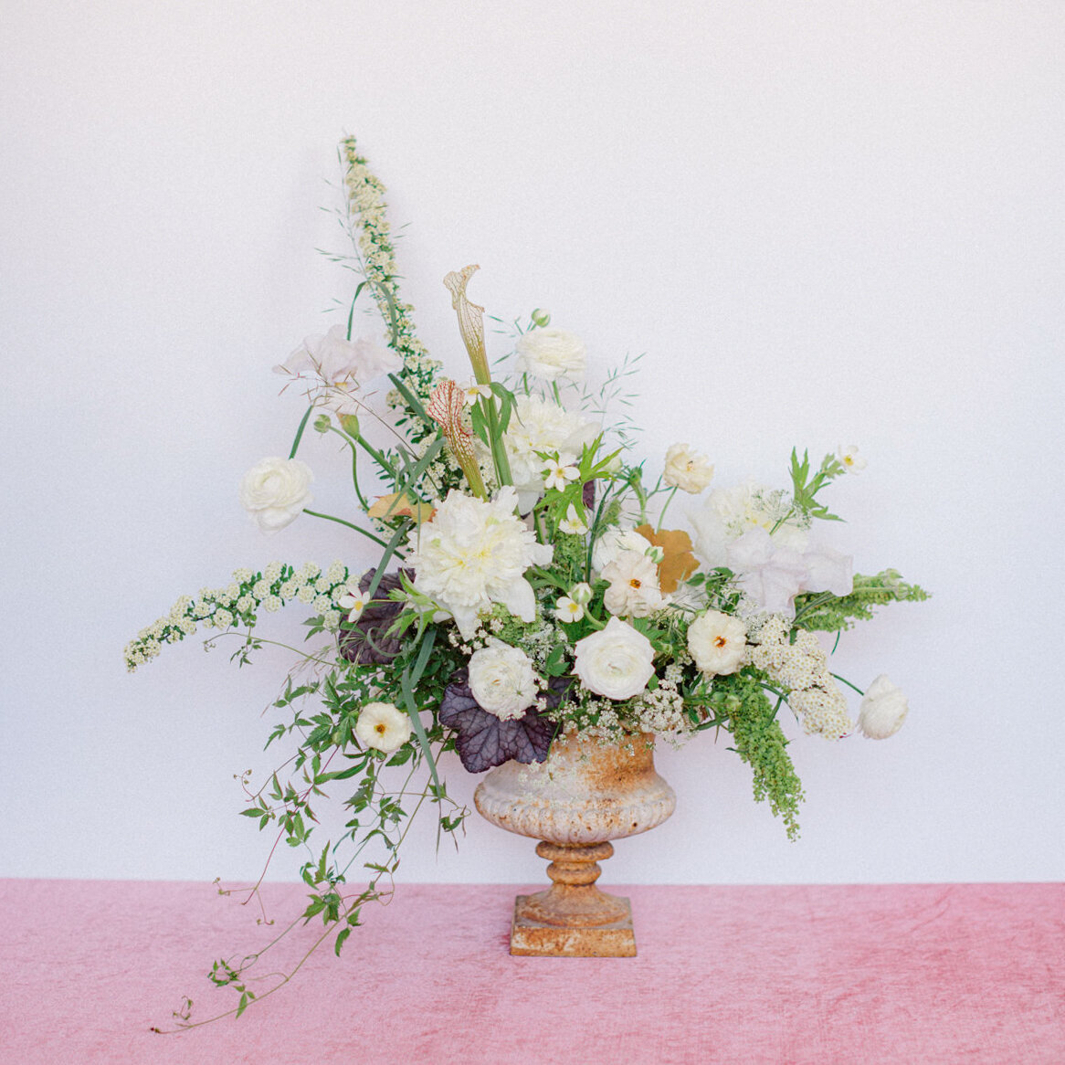 A large springtime flower arrangement sits in an urn on a pink floor at a Montreal wedding. 