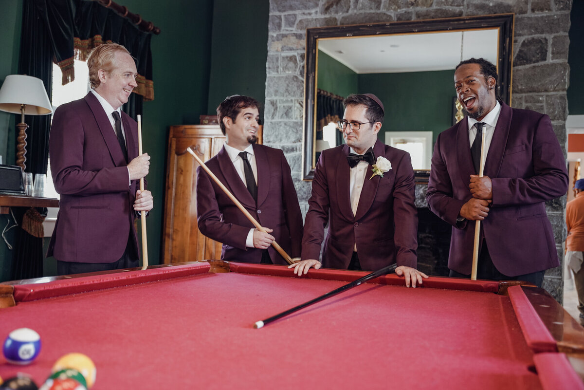 Groom and all his groomsmen stand around a pool table dressed in purple blazers at Belmont Country Club