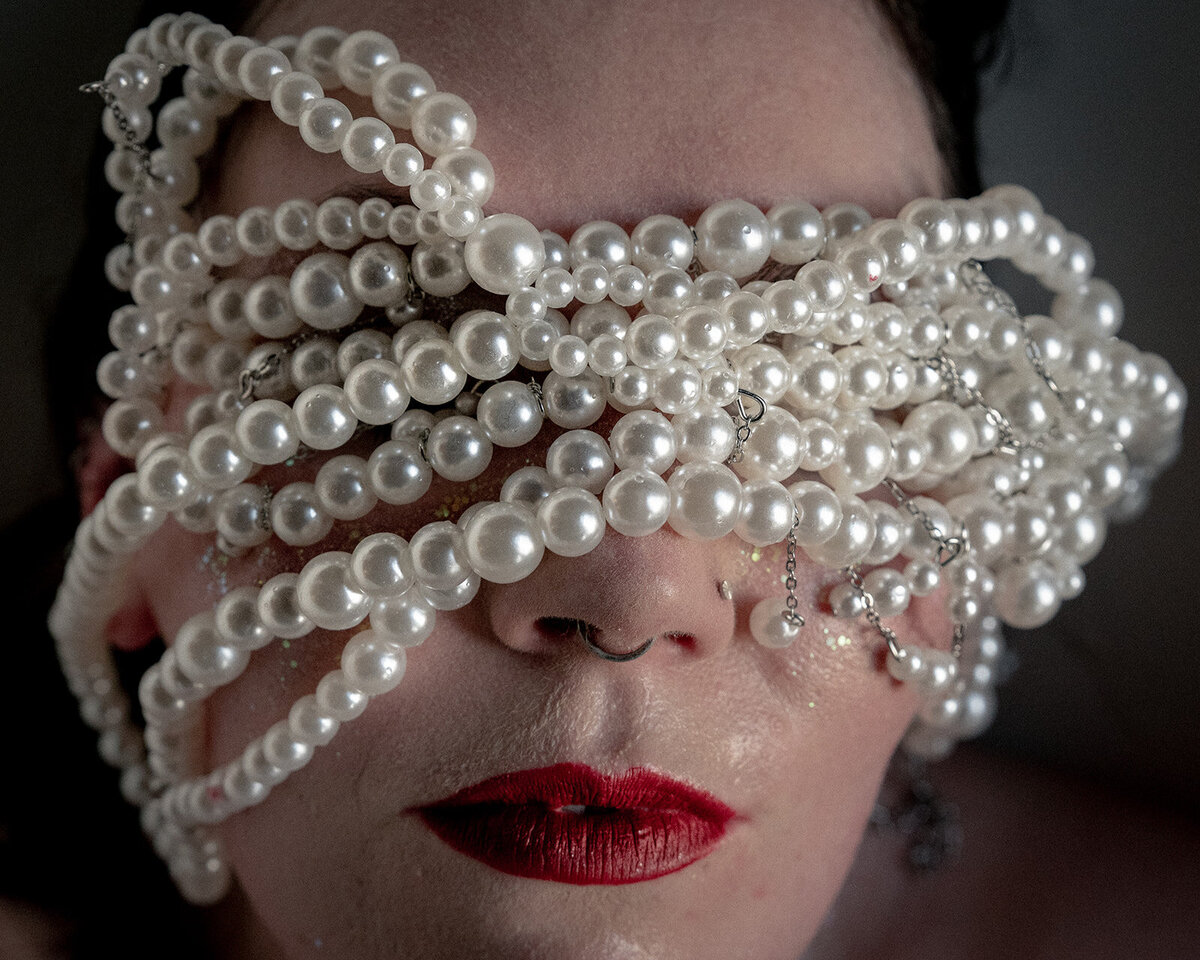 Intimate boudoir photo shoot, bride with red lips and her face wrapped in pearls.
