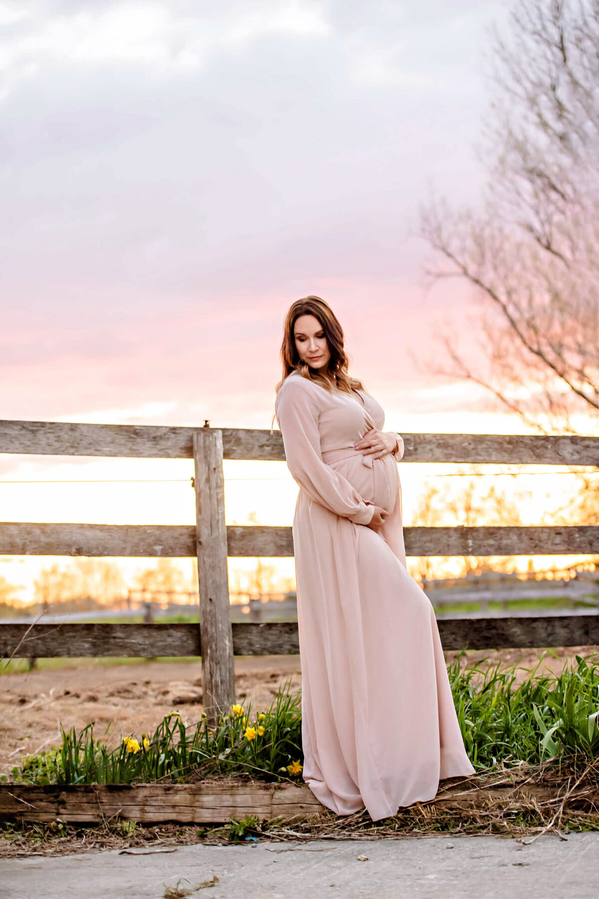 pregnant woman in front of a fence with a pink sky in the golden hour for her outdoor maternity photography session in Burlington, Ontario