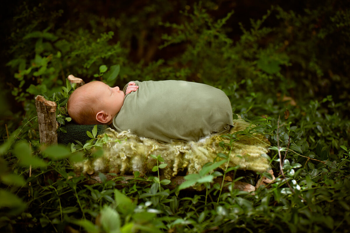 Newborn swaddled in an outdoor green garden on a rustic bed-inspired backdrop in Overland Park, Kansas. A perfect scene for families wanting earthy and creative newborn photography.