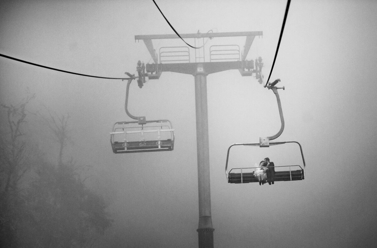 A mystical and serene scene with two ski gondolas emerging from a dense fog, with a lone couple visible in the nearest gondola.