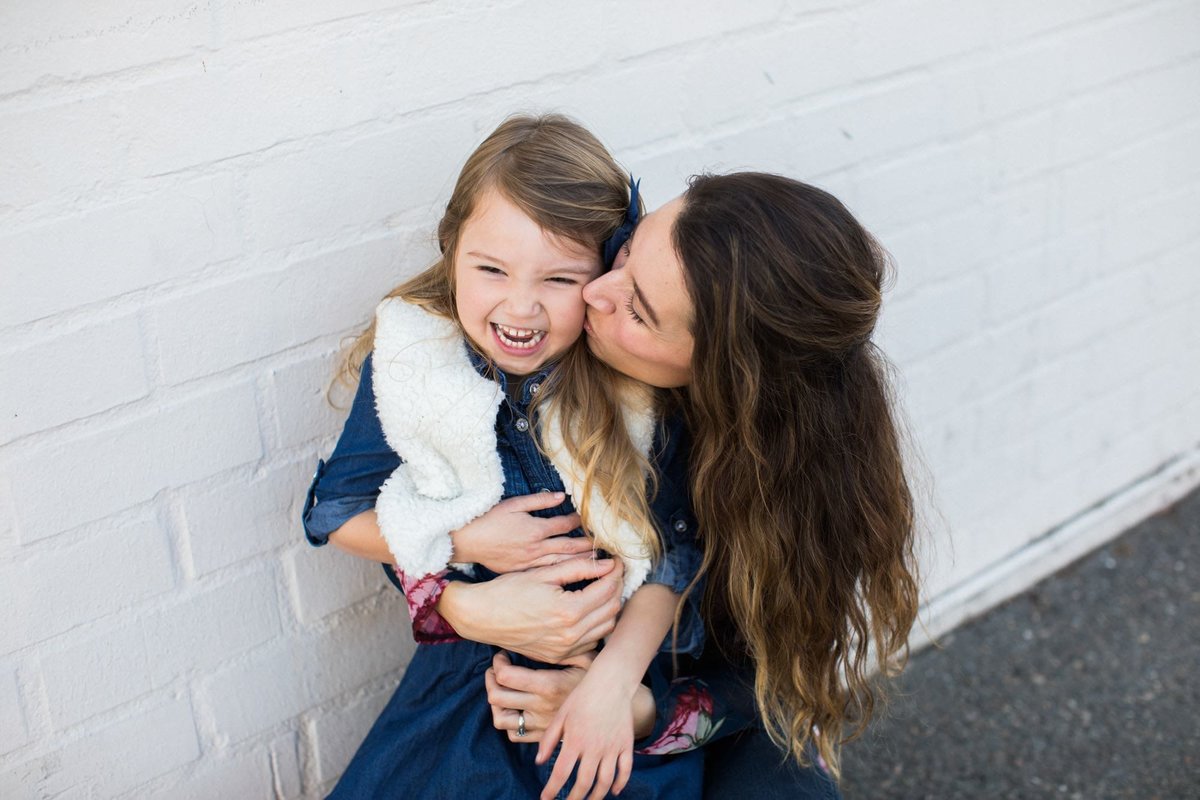 A young girl giggles while mom kisses her on the cheek