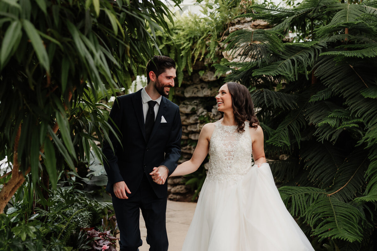 A wedding couple runs through the plants laughing at Wilder Park Conservatory.