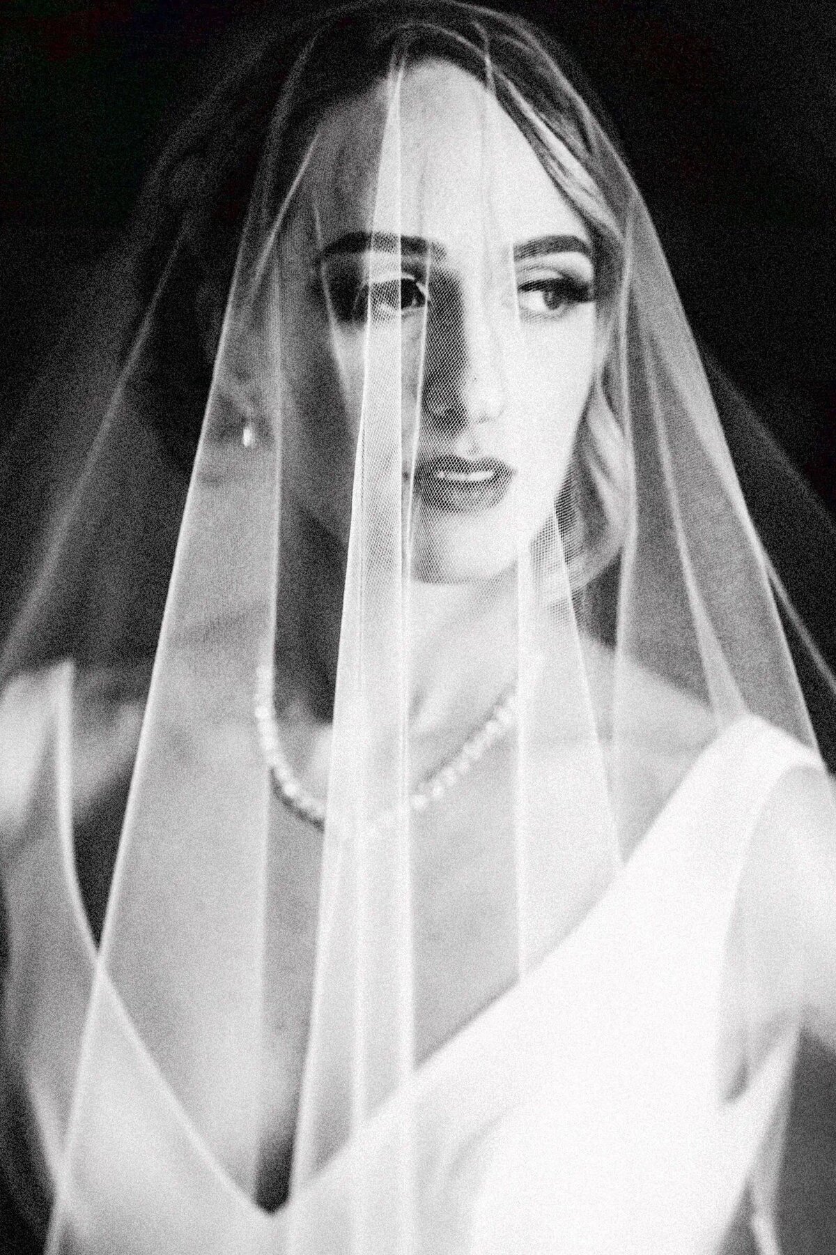 Portrait of a bride with a focused gaze through her sheer veil, highlighted in a grainy black and white photograph