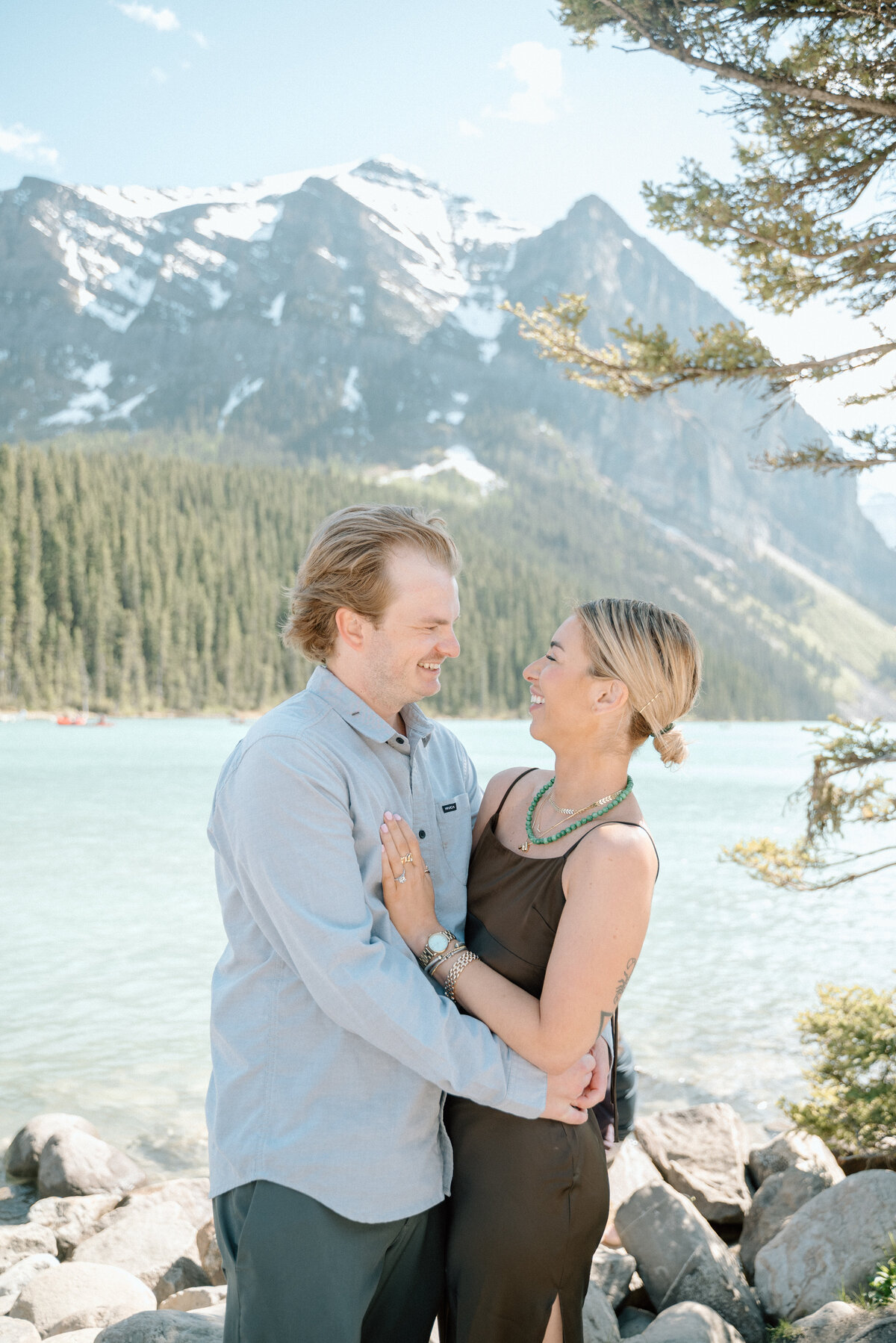Couple hugging in front of Lake Louise with dreamy mountain reflections.