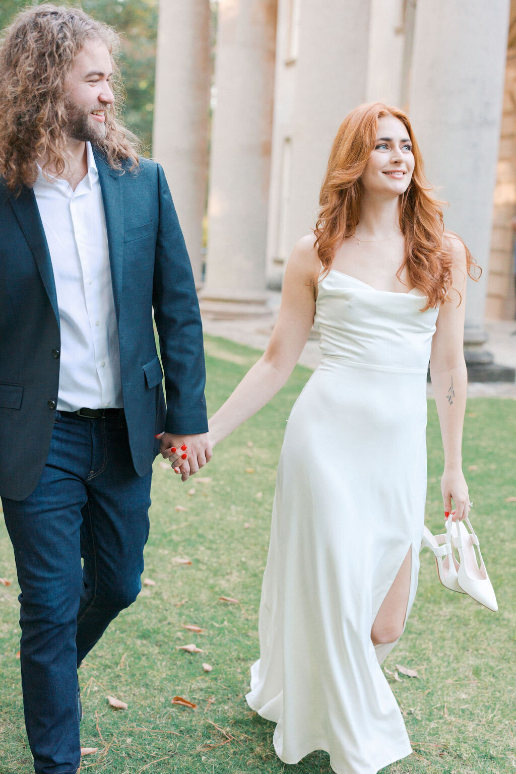 Bride and groom hold hands and walk on the grass of the Swan House front porch