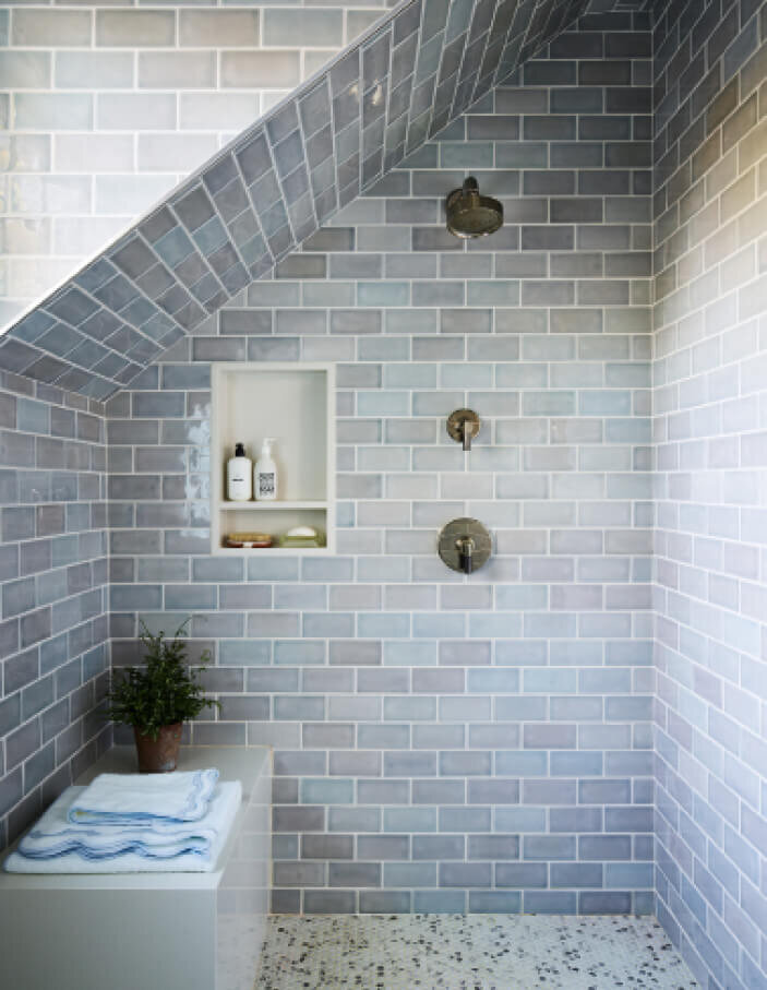 Light blue tile shower design by a Boston decorator features Kallista plumbing fixtures and a custom stone bench, blending luxury with timeless craftsmanship.