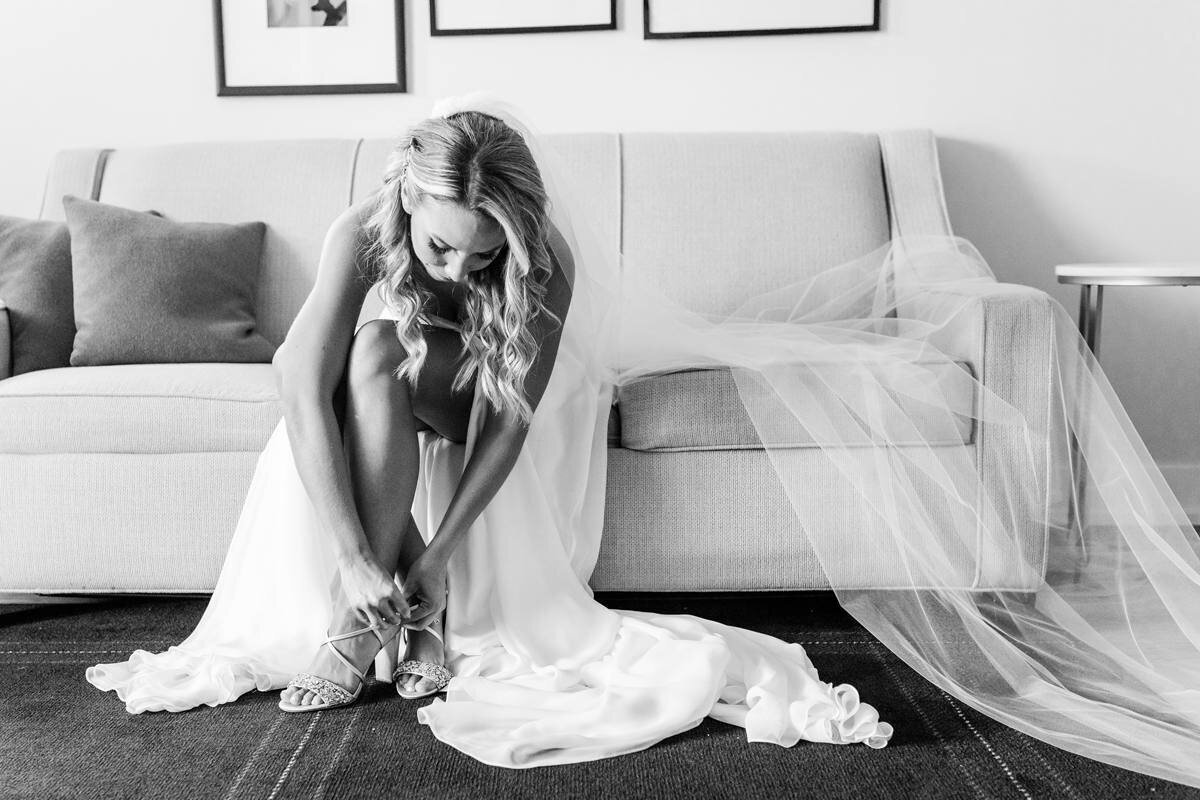 timeless black and white photo of bride putting on badgley mischka bridal shoes