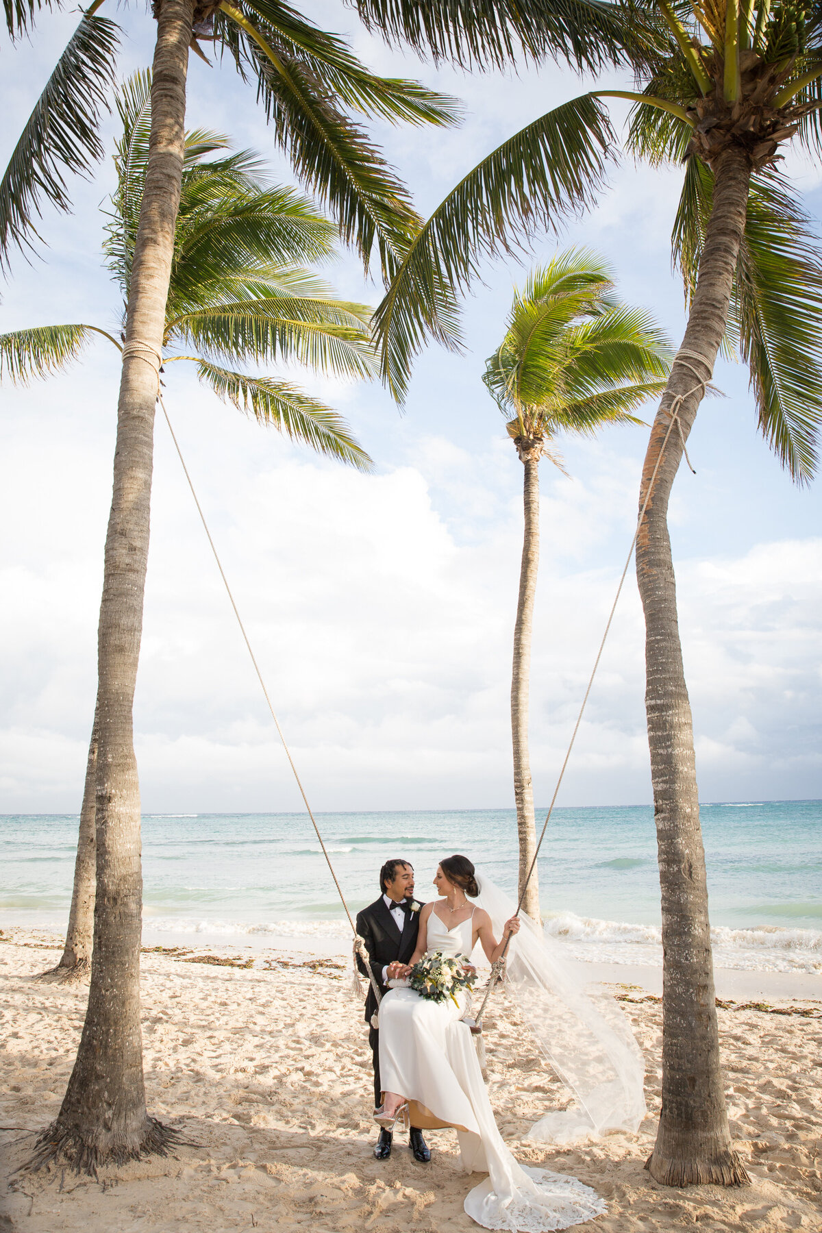 Austin wedding photographer captures a stunning moment of a bride and groom playfully swinging on a swing on the beach.