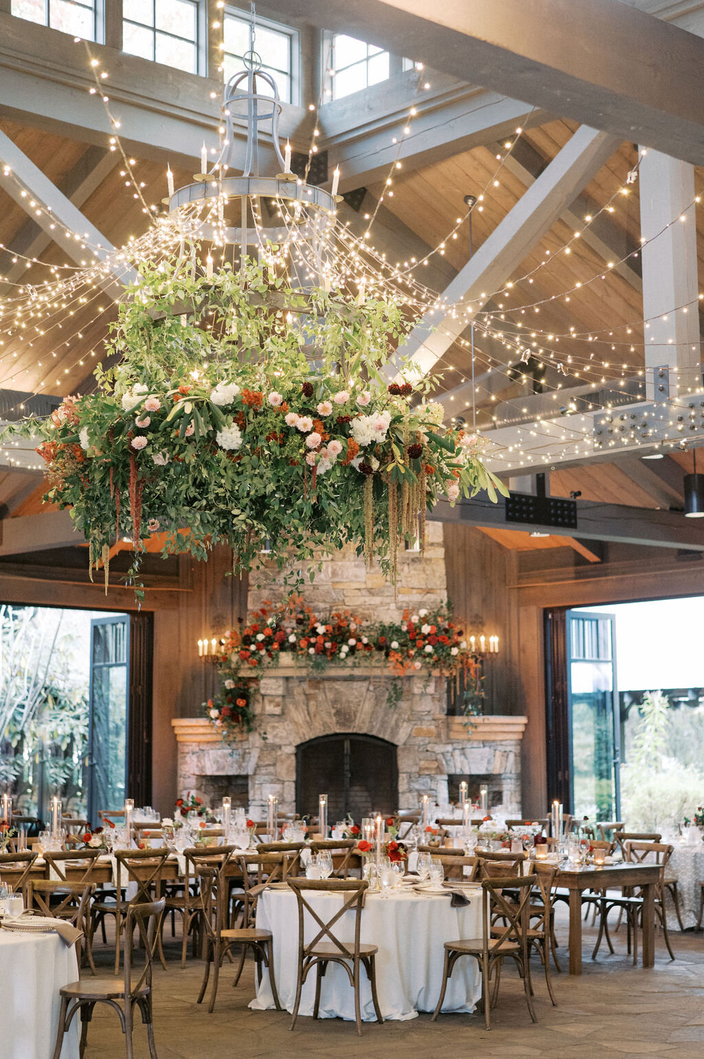 Luxury wedding reception with long tables, bud vases and taper candles, stone fireplace with red floral arrangements and large hanging chandelier installment at Old Edwards Inn in Highlands, NC. 