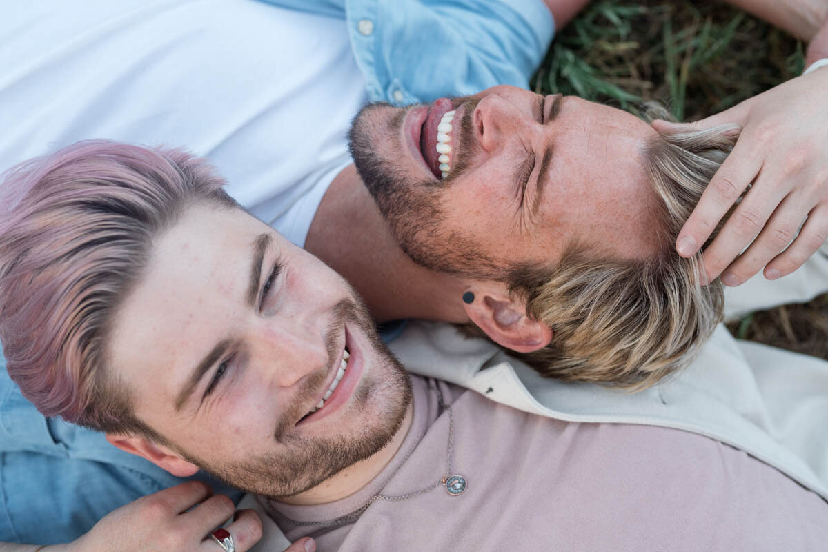 Men snuggling while laughing and laying in the grass