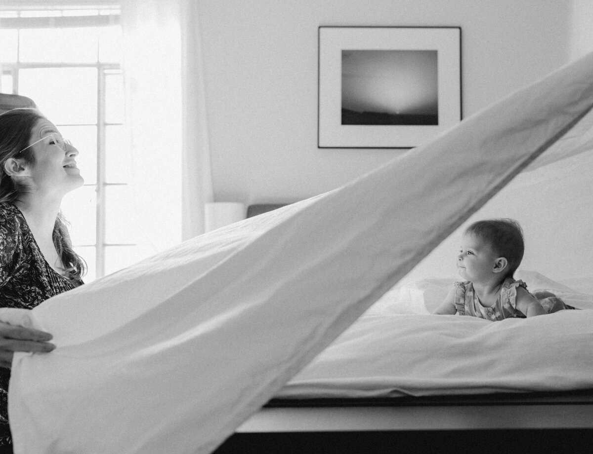 Mother throwing sheet in the air with toddler on bed