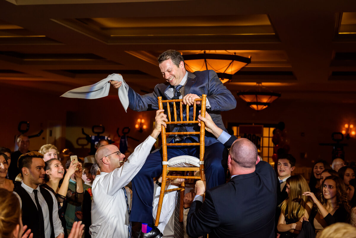 A man is lifted up on a chair by a group of people on the dancefloor