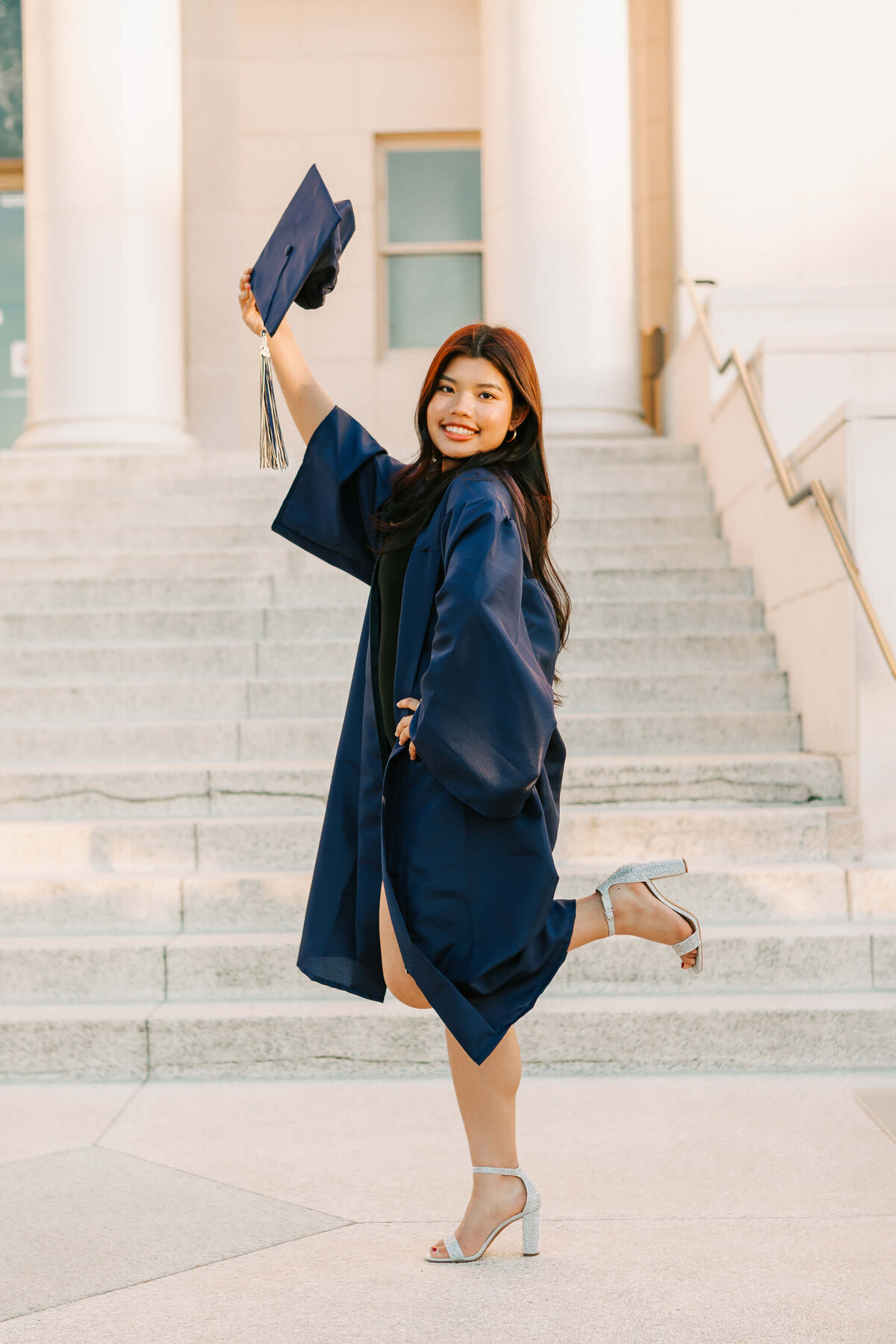 A high school senior stands in a blue gown holding her cap downtown Albany, OR