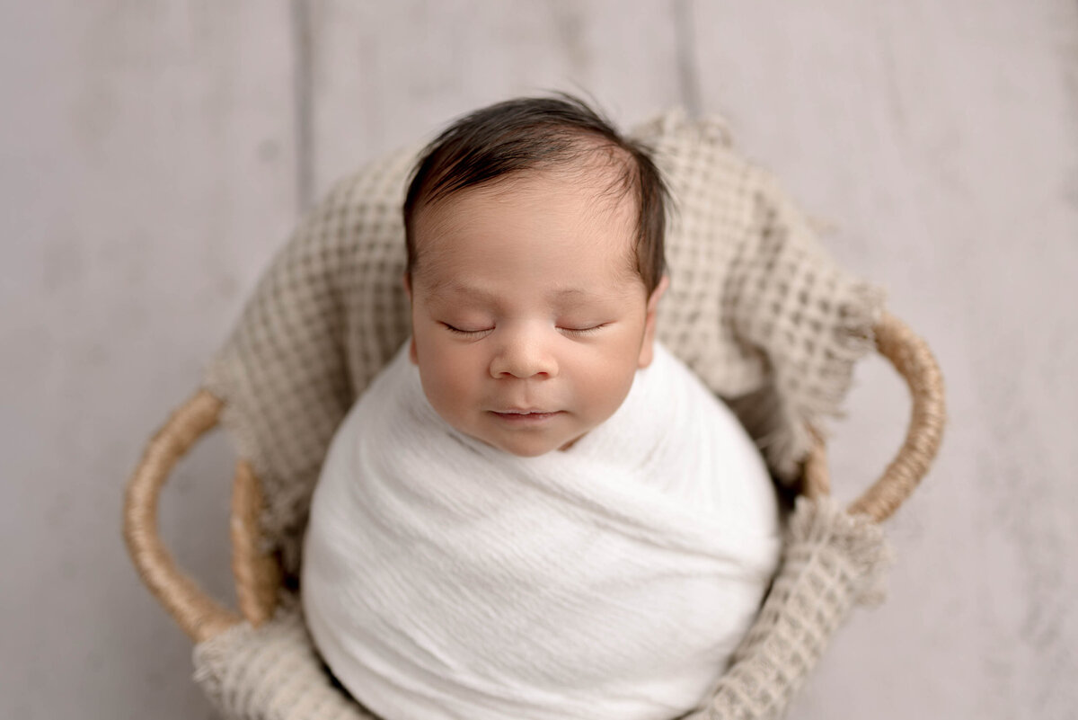 Baby boy wrapped in white swaddle and placed in a whicker basket