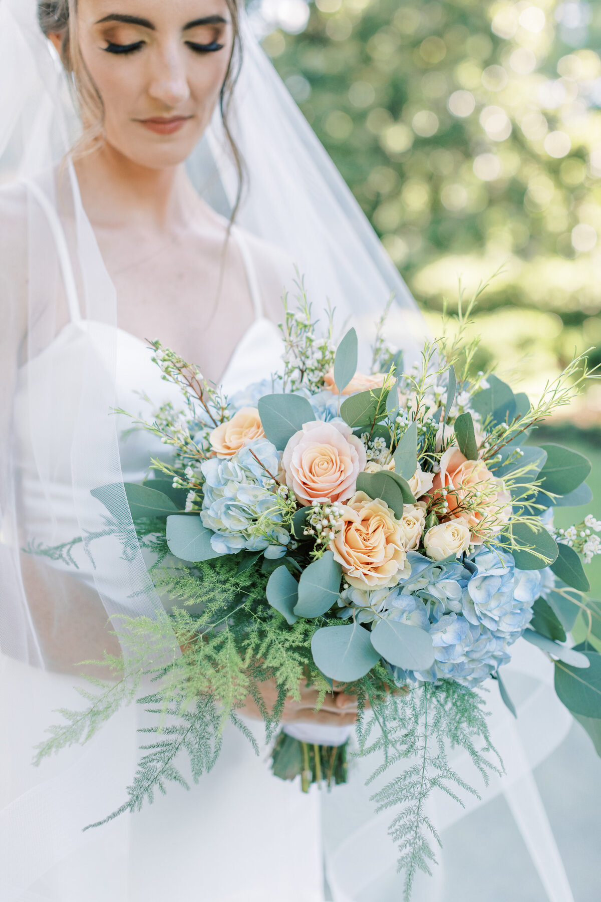 A bride holds her peach and blue bouquet.
