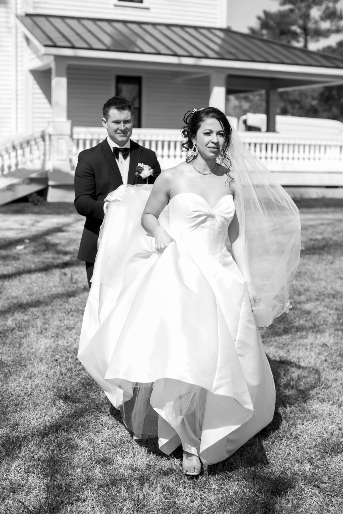 groom holding bride's dress while him and his bride are walking, wedding venue in the distance