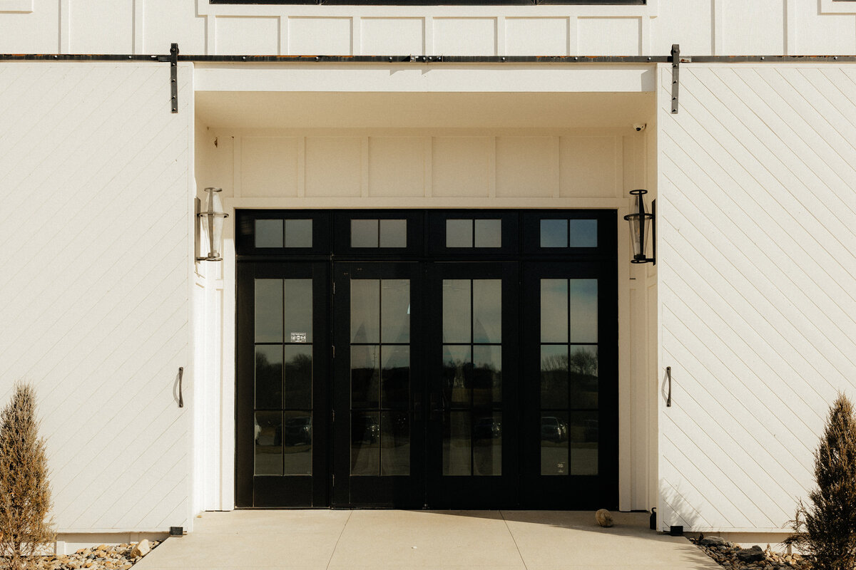 The front doors of the wedding venue which are black window pane doors.