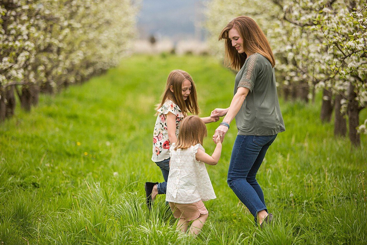 Mother and daughters holding hands and twirling in orchard