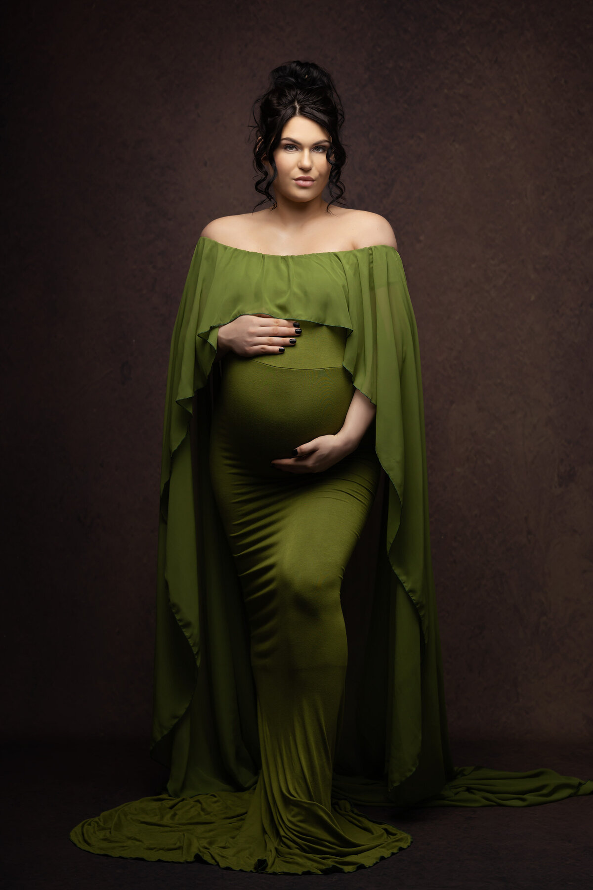 DFW maternity photography of woman in a flowing green gown, hands gently resting on her belly.