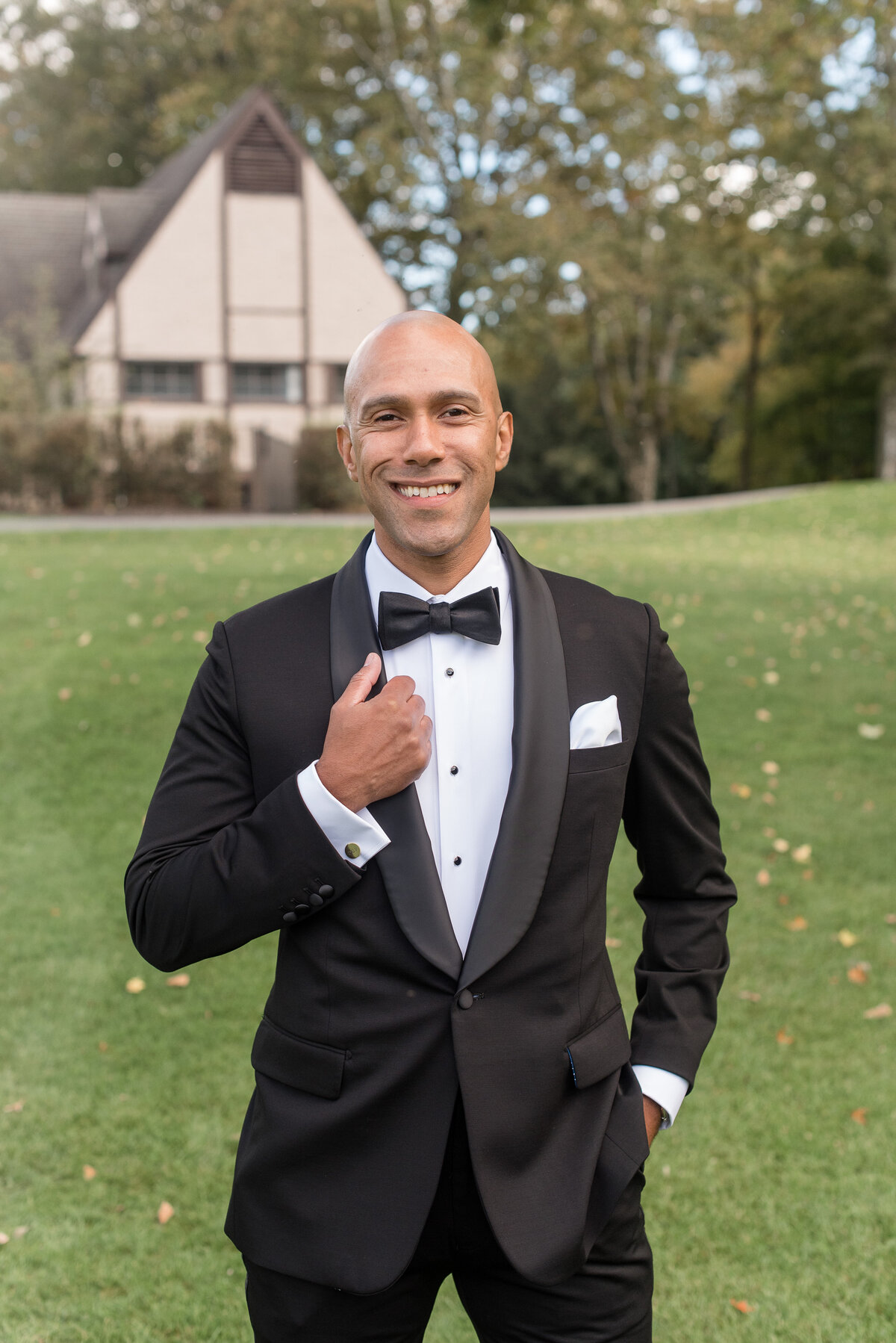 Groom smiling at camera holding edge of black tux jacket with right hand in North Jersey.