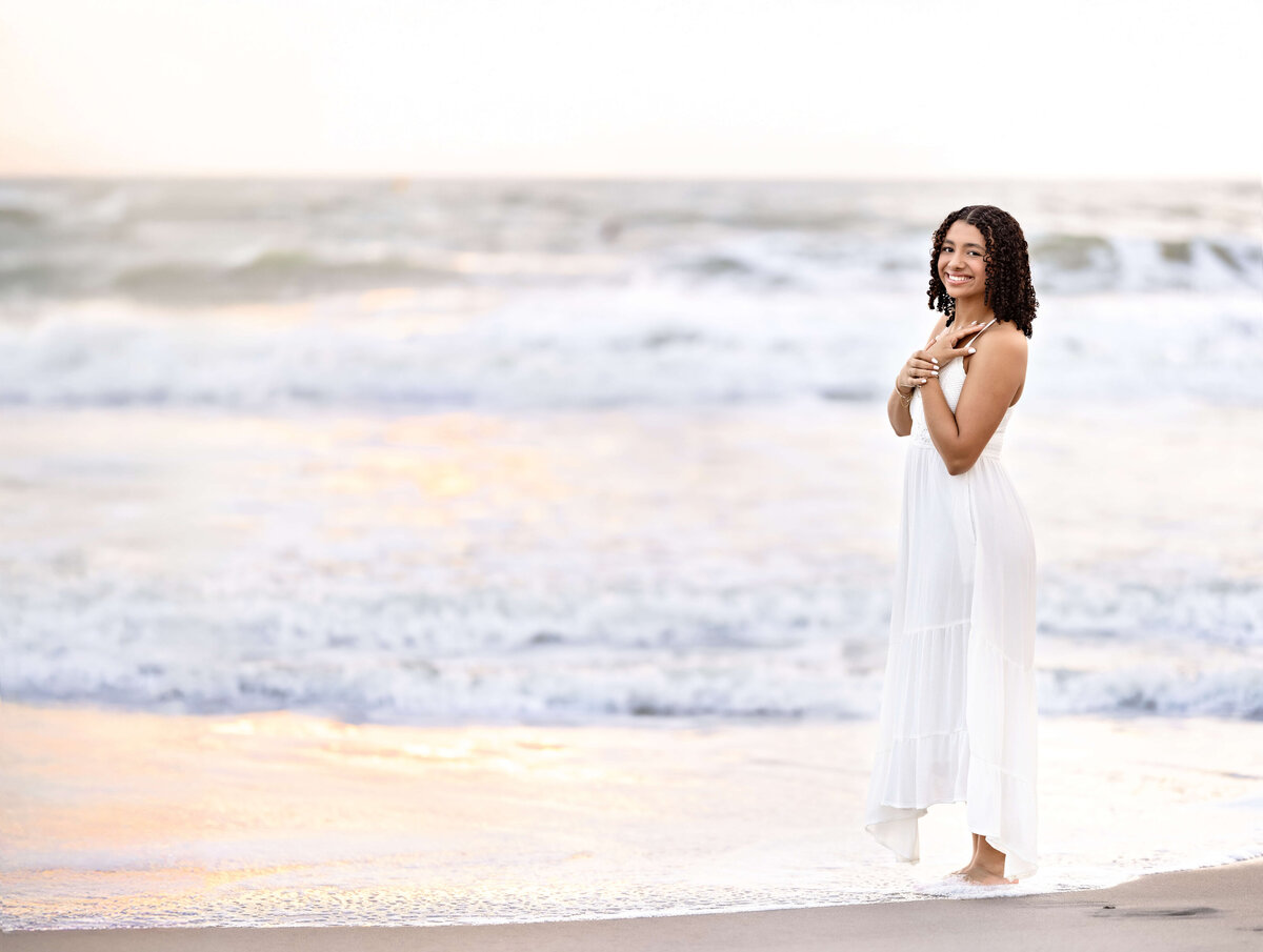 Cocoa Beach senior portraits with a teen girl softly gazing toward the camera, positioned off-center with ocean in the background. 