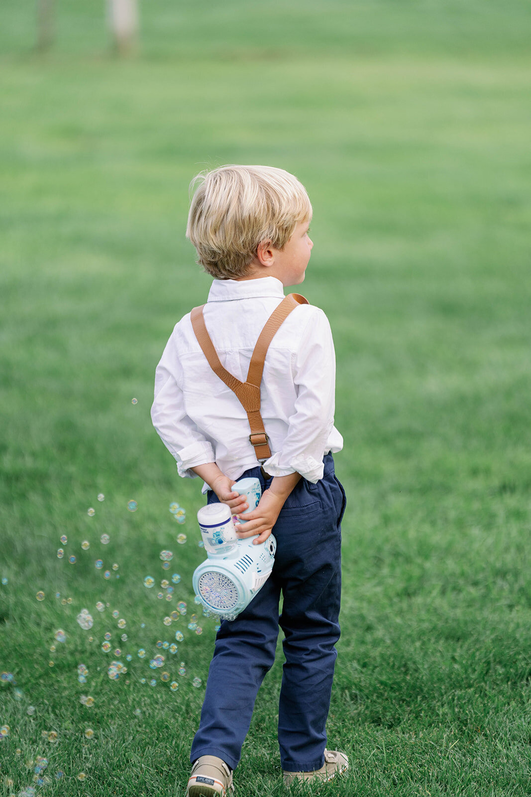 Cute candid photo of a child holding a bubble gun behind his back, ready to spray bubbles during a fun fall orchard wedding at Nugent Orchards.