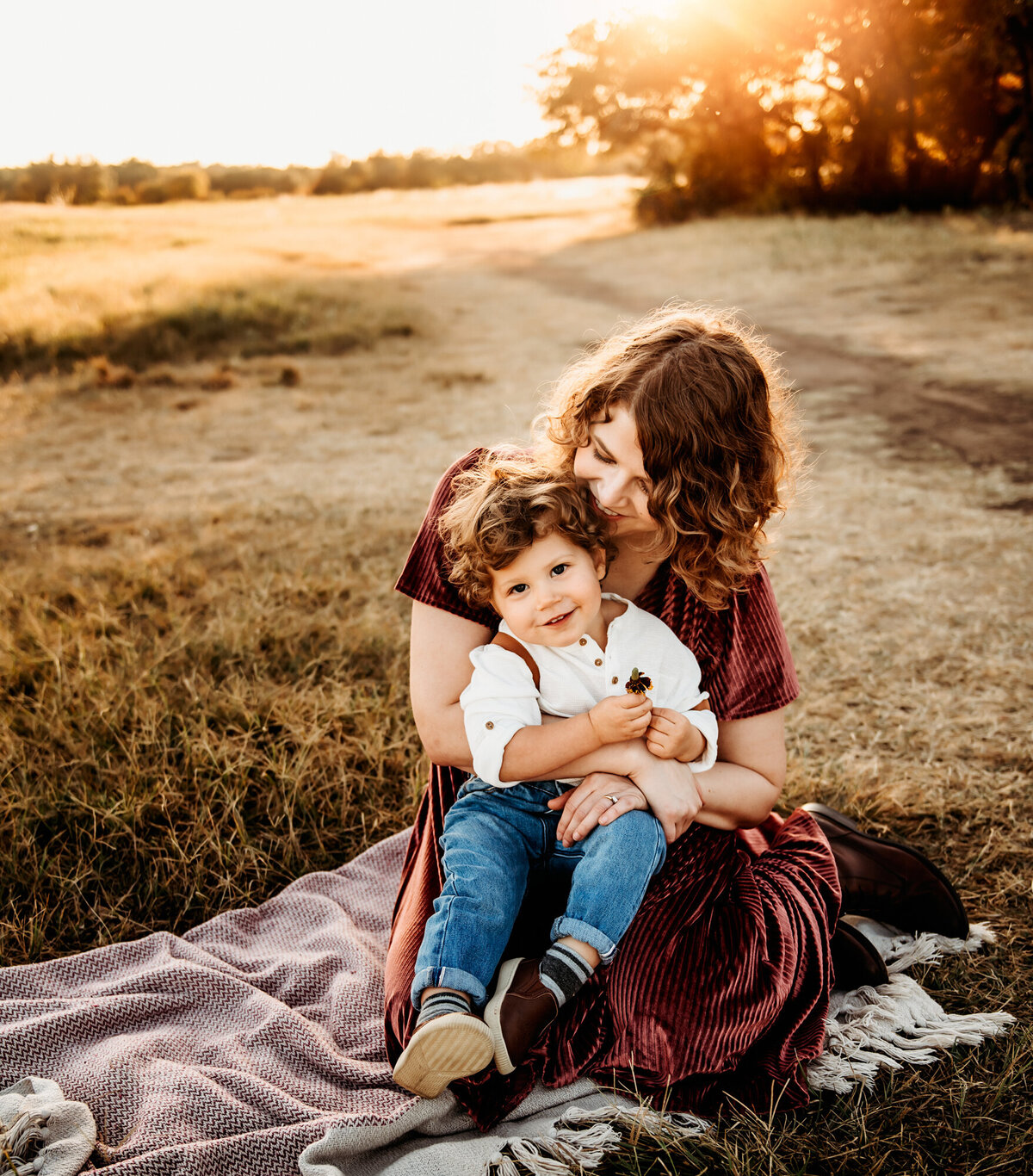 Mom kissing little boy on a blanket in the sunset.