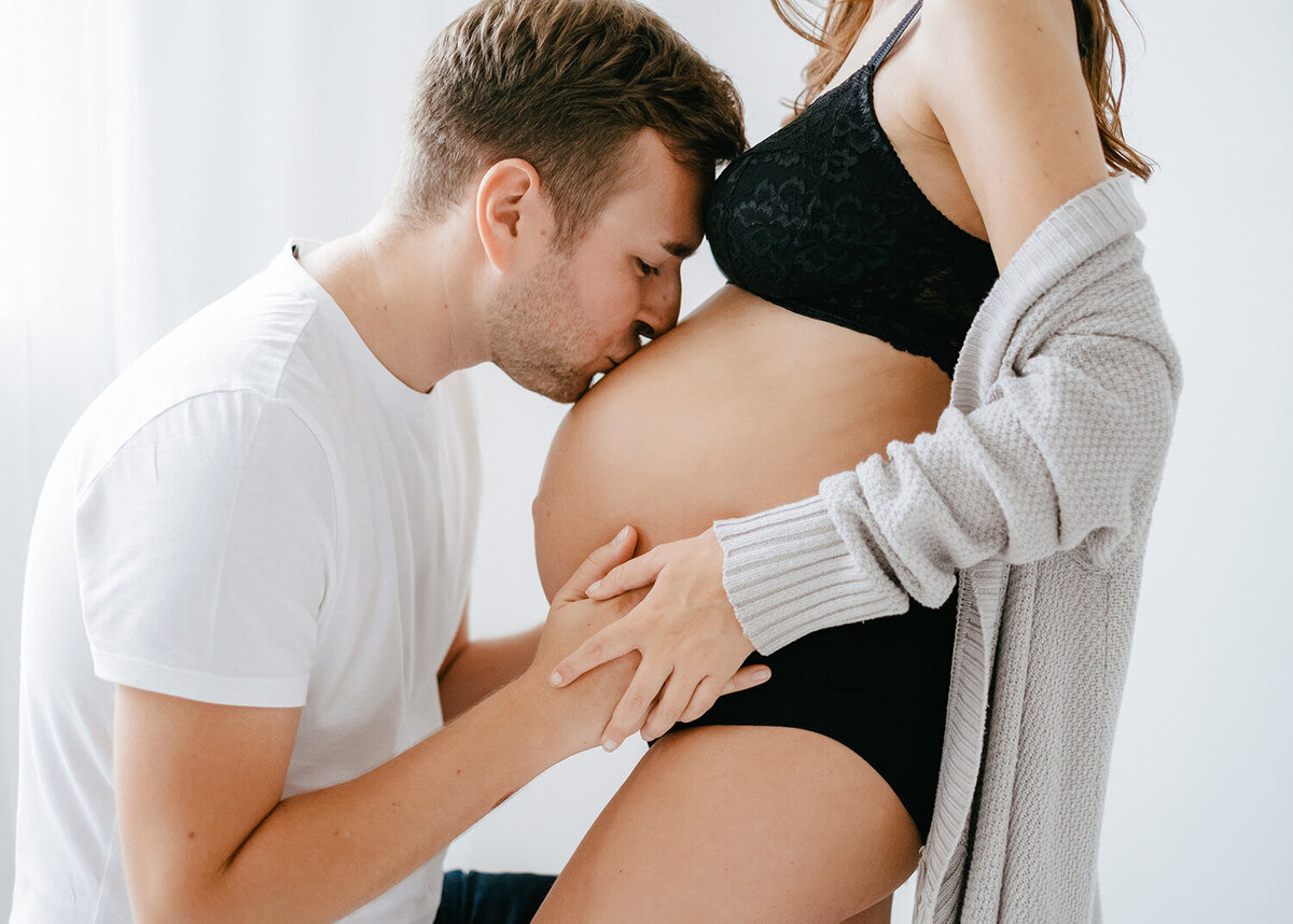 Couples maternity shoot in a studio where a man kisses his partner's bump