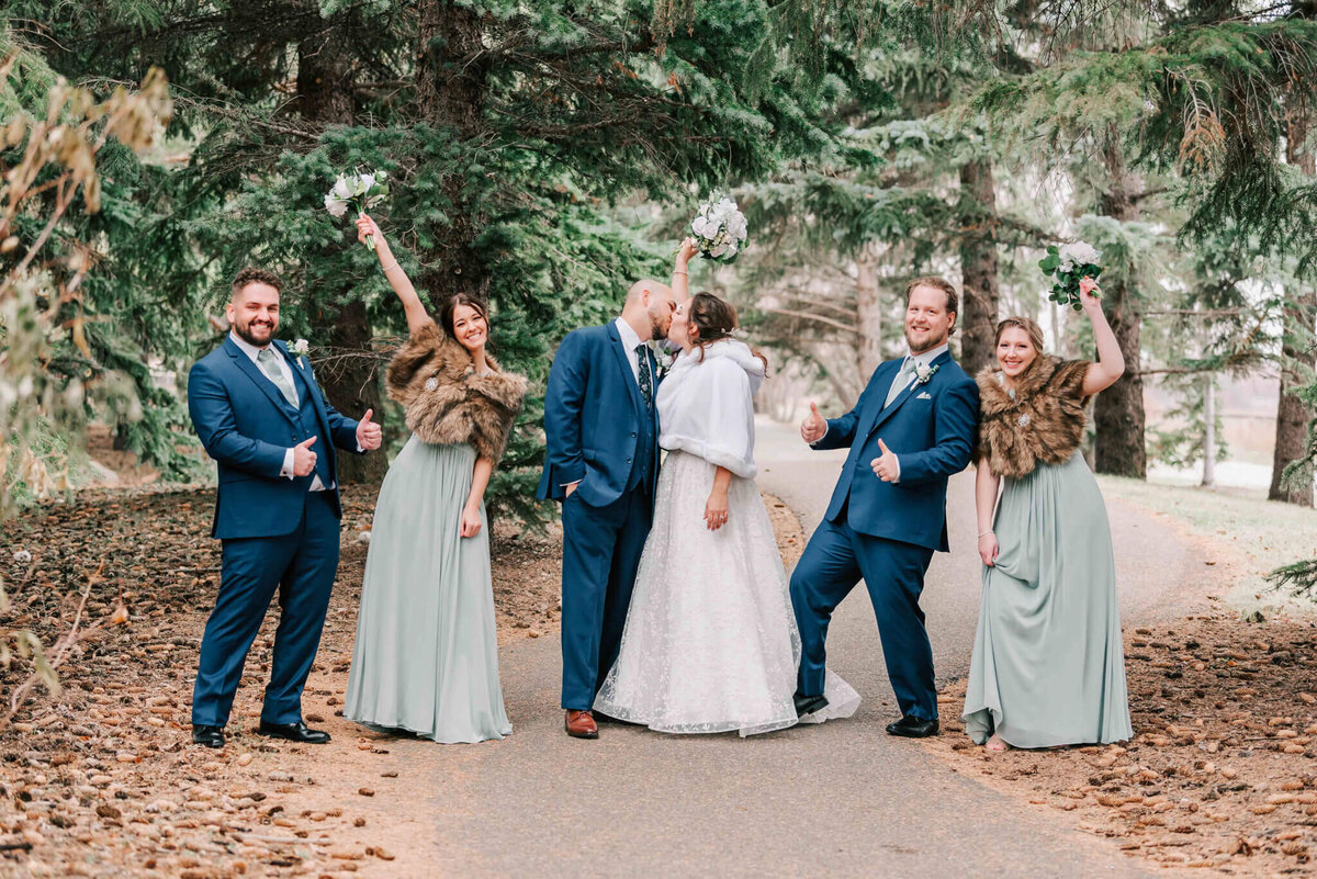 Bride and groom share a kiss standing in the middle of their bridal party.
