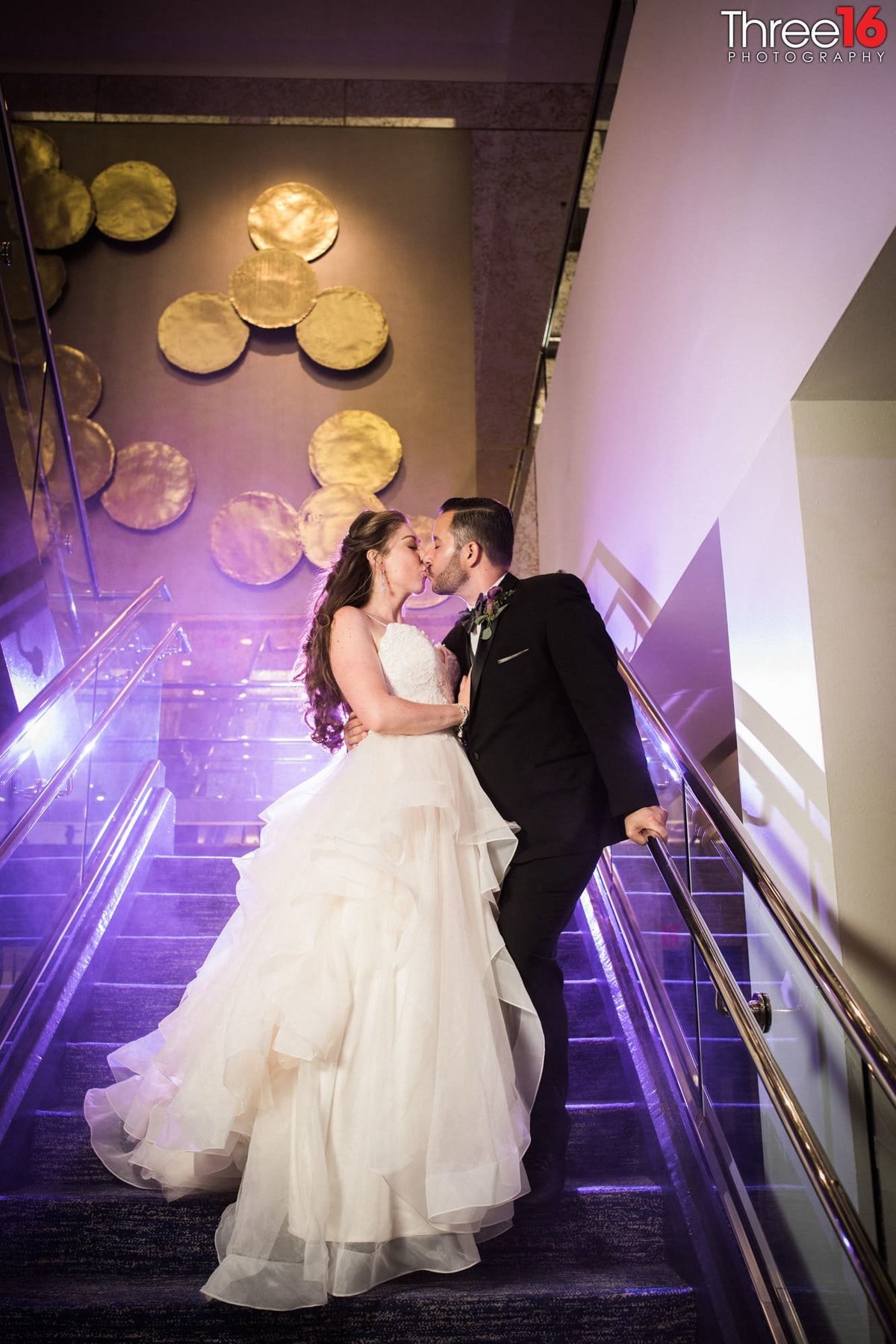Bride and Groom stop for a kiss on the stairwell with purple hint behind them