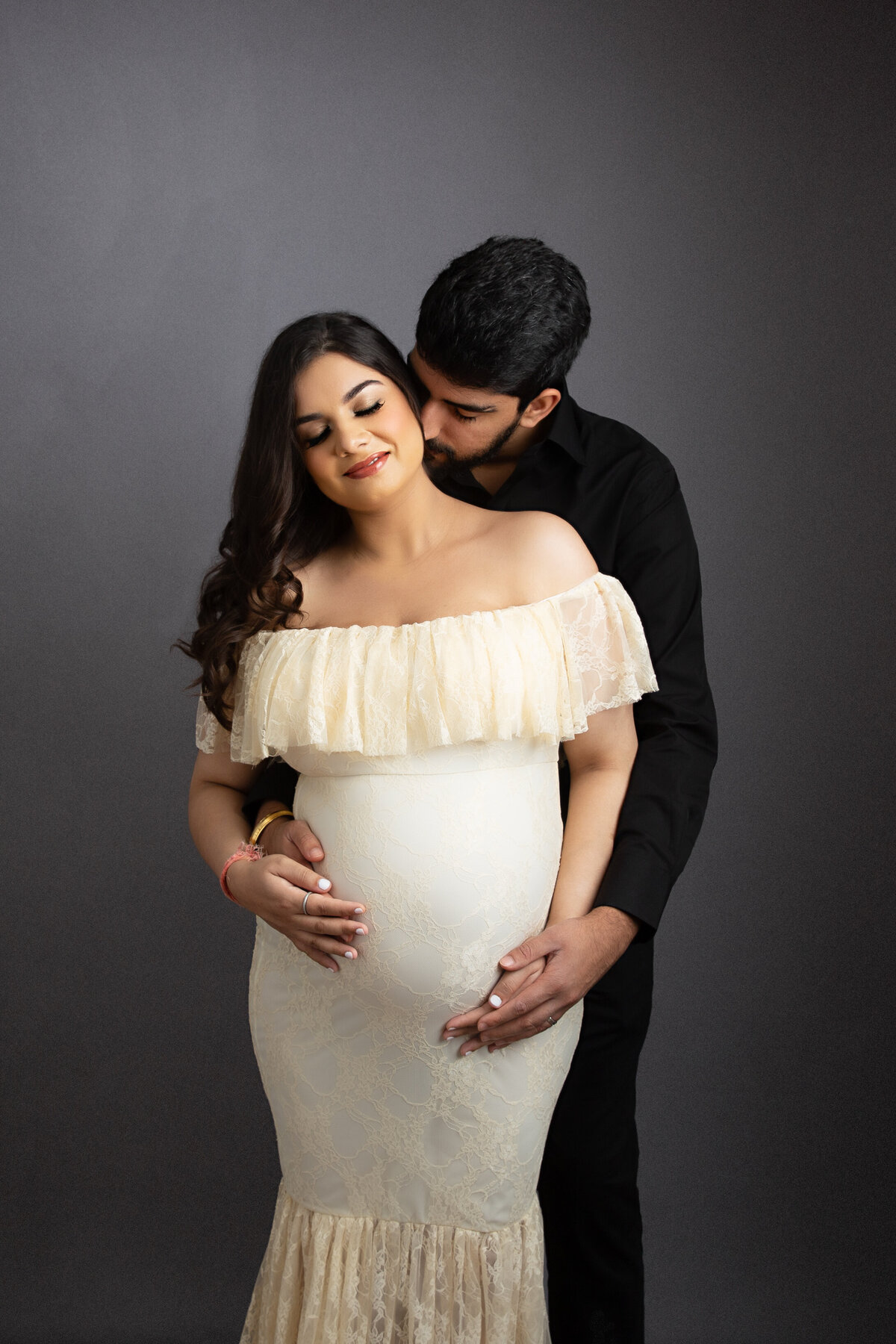 Husband embracing his pregnant wife from behind and lovingly kissing her on the neck.