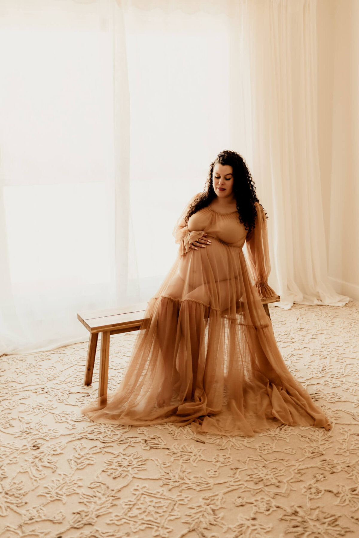 Woman wearing a Reclamation gown sitting on a bench and looking at her belly, Edmond, Oklahoma maternity session.