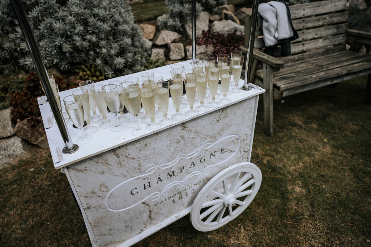 A white cart filled with wine glasses on top of a grass covered field