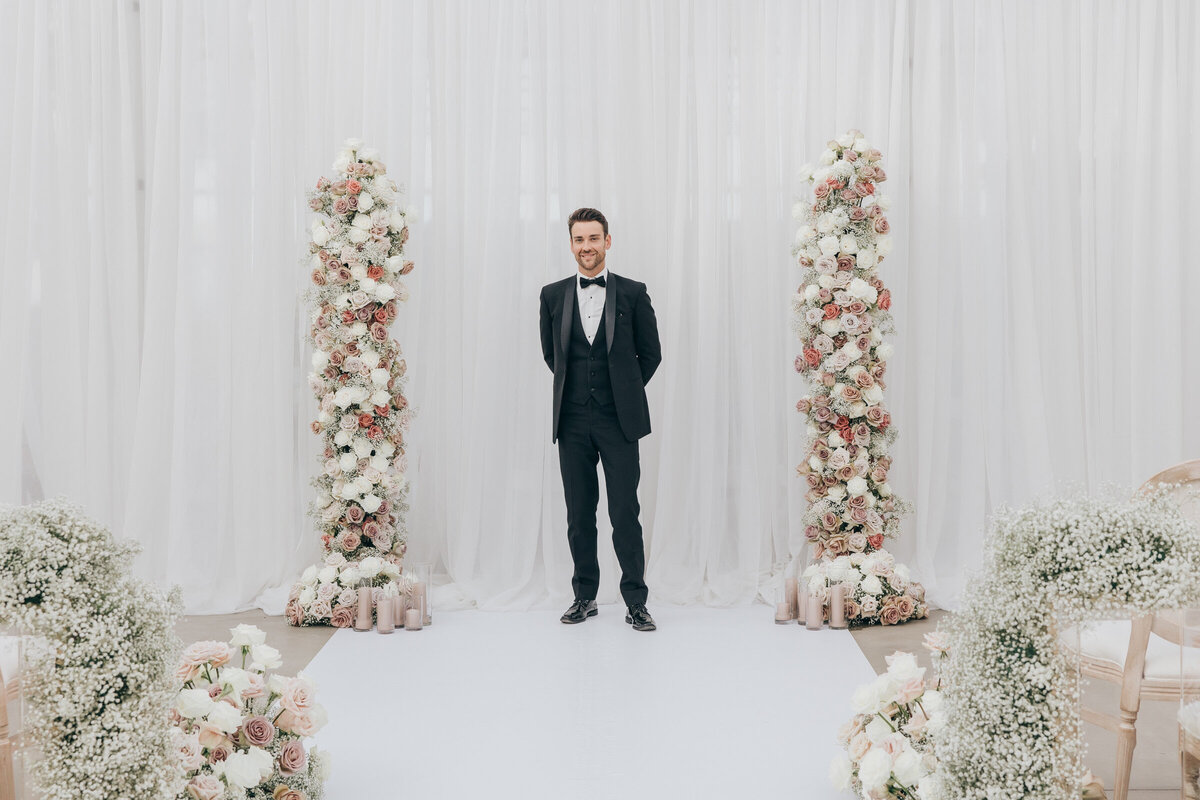 Floral designer standing beside rose wedding arch