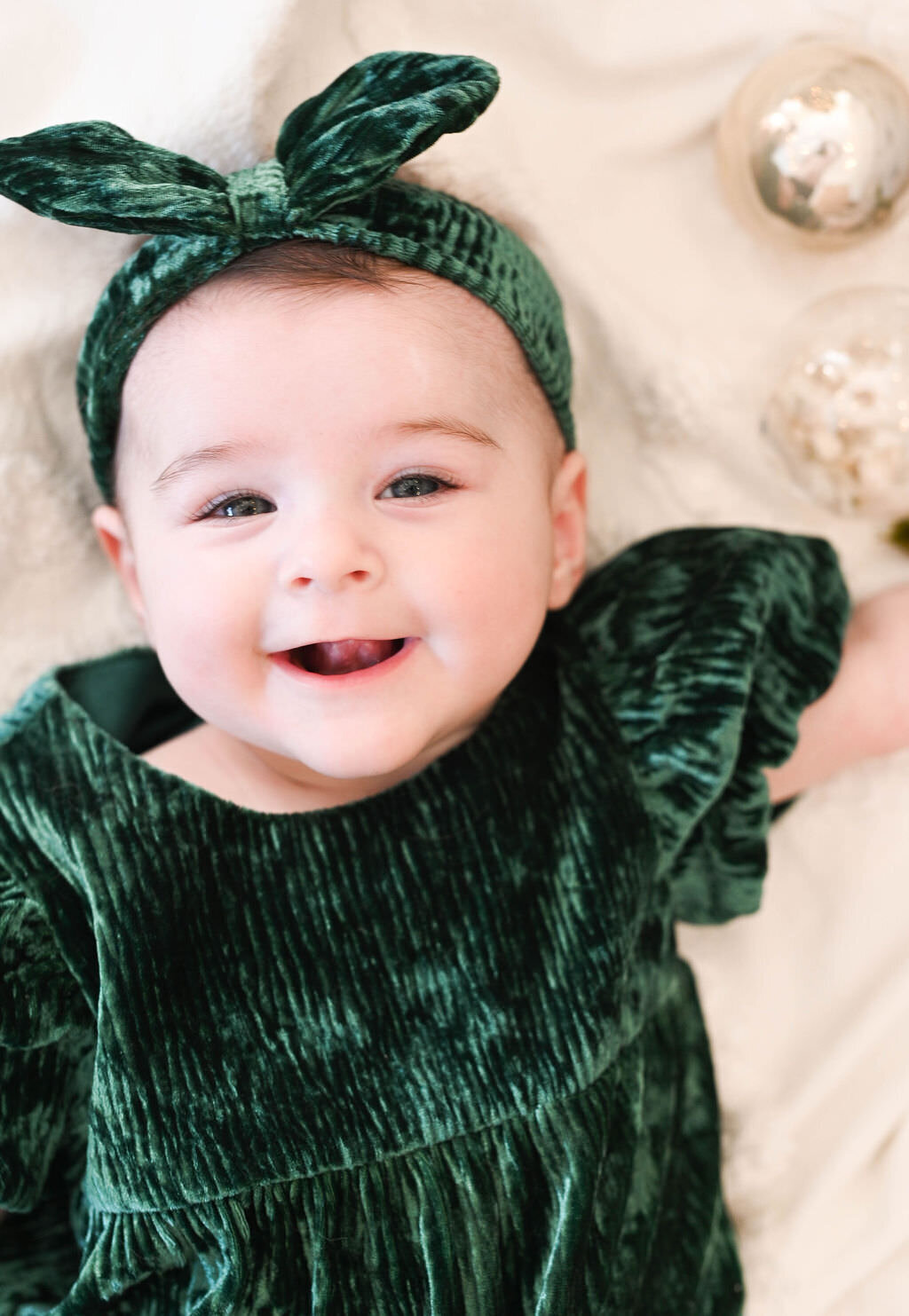 A small child smiling in a green velvet dress and bow.