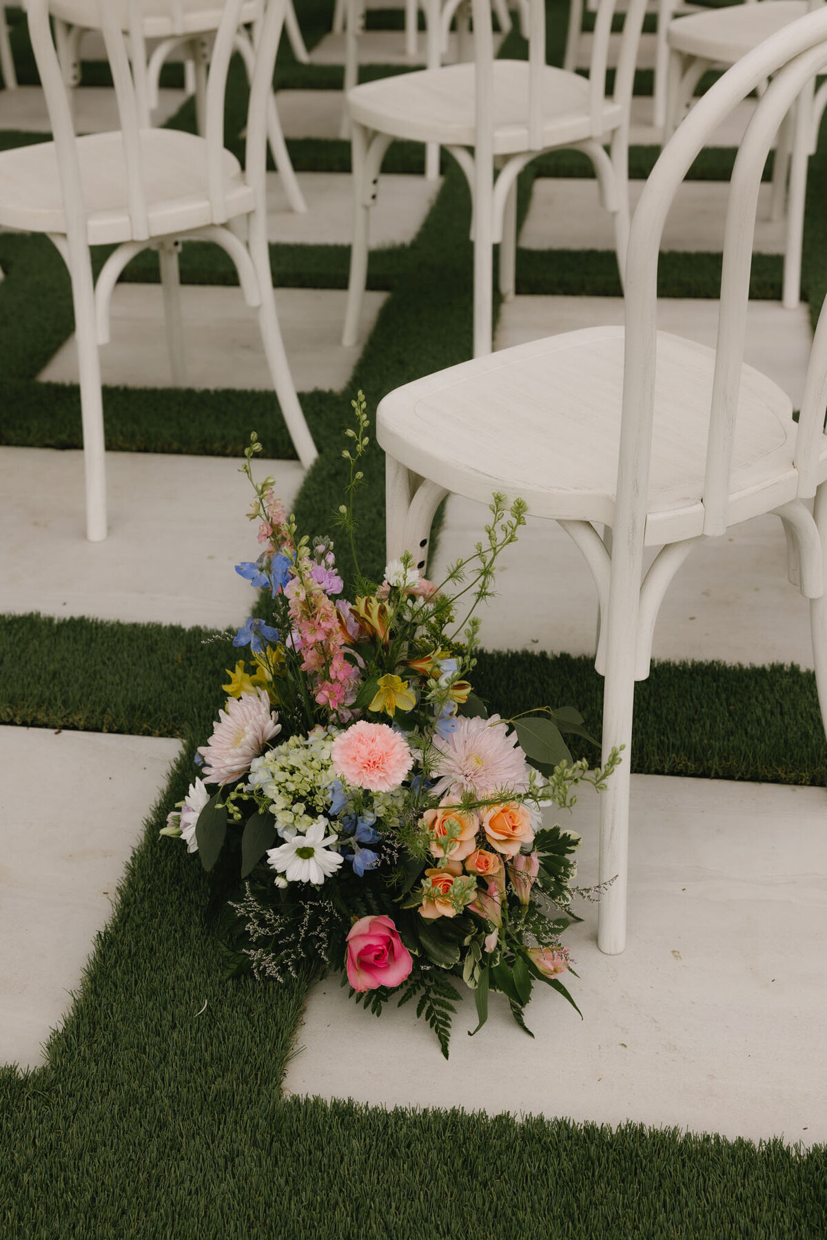 Aisle flowers beside white chairs on green turf