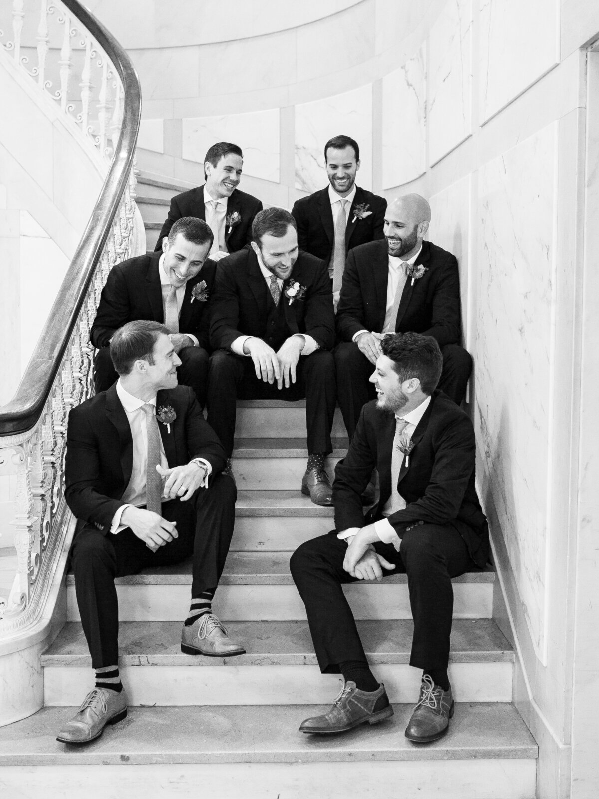 The groom laughs with the groomsmen in a stairwell.