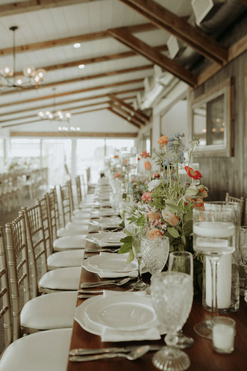 cut glassware and white china with elegant silverware on feasting tables with blush and coral and white wildflowers in the reception space of the Willowbrook wedding venue