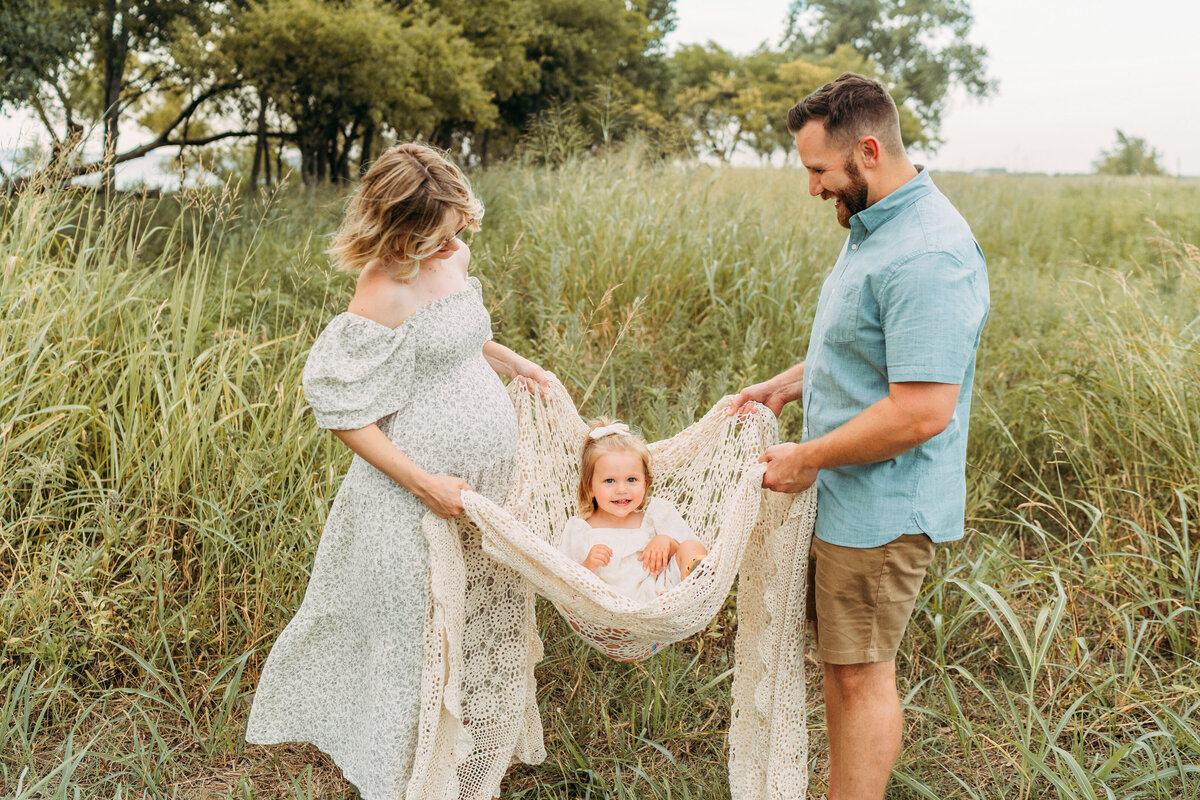 dad and pregnant mom swing their little girl in a blanket