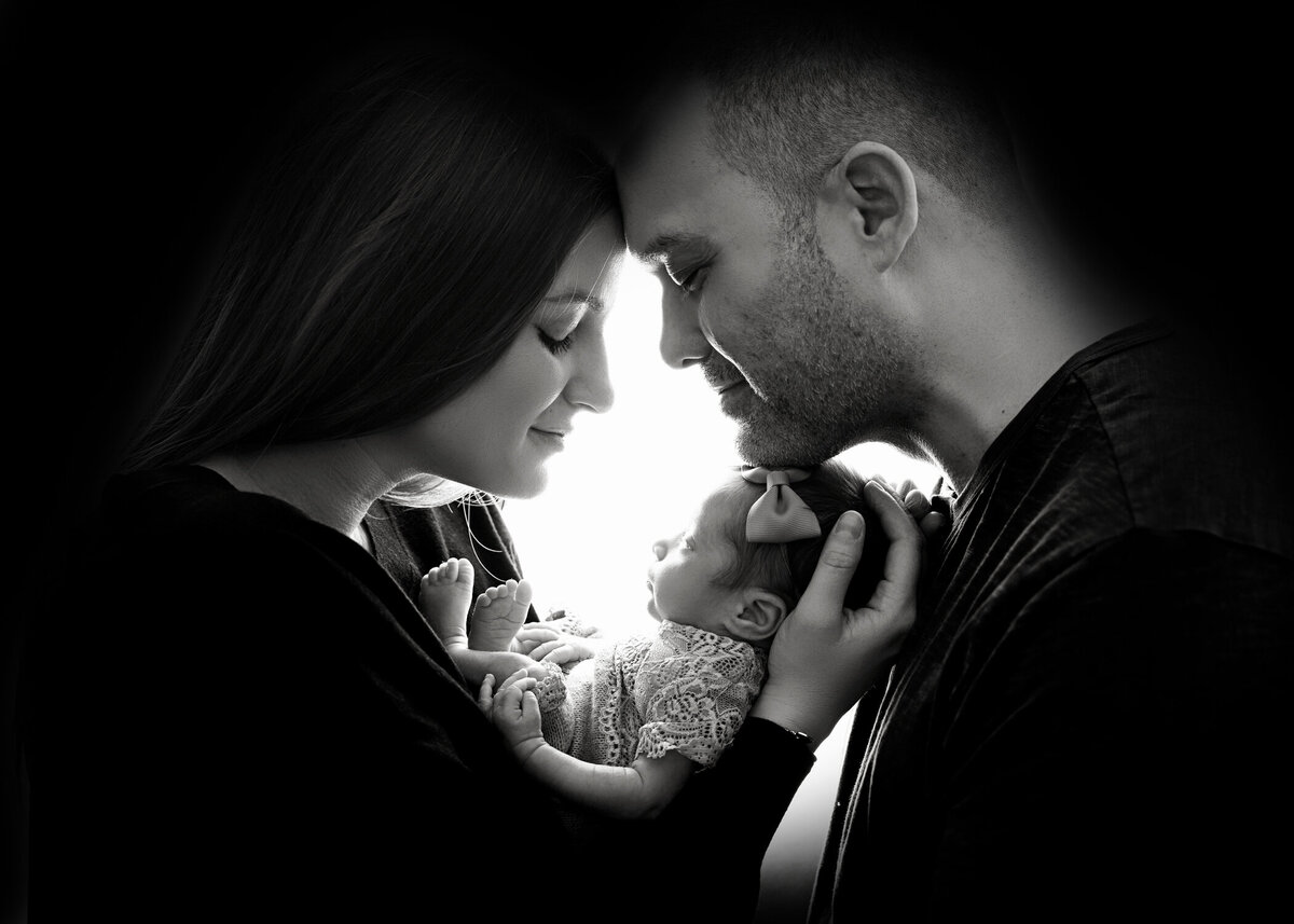 A black and white image on happy new parents touching foreheads above their sleeping newborn daughter during their NJ Newborn Photography session