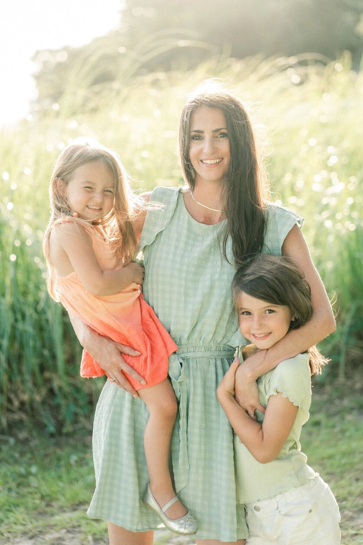 A mom holding one kid in her arm with her other arm over another child's shoulder.