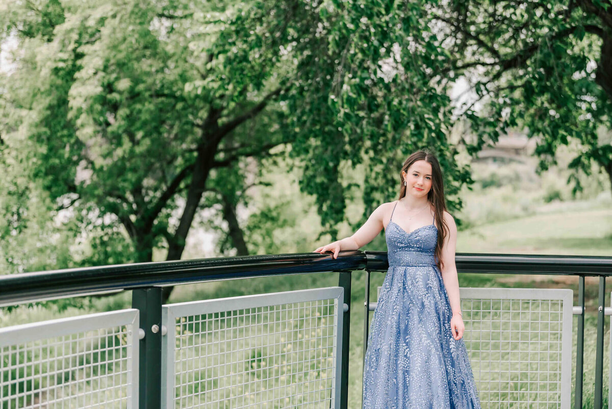 Girl in purple dress standing by a railing with trees.