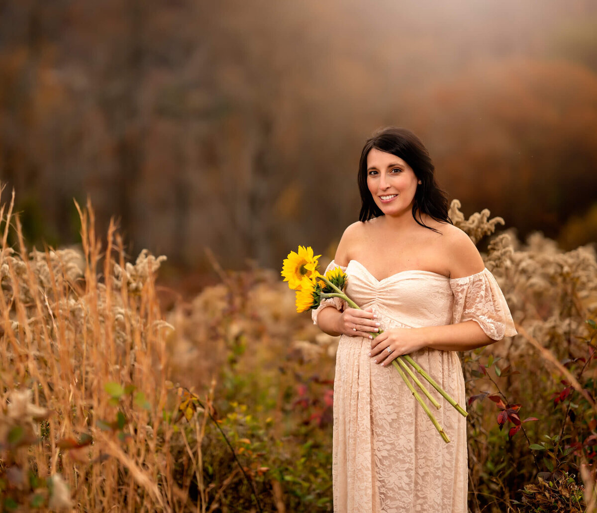 A lovely young expecting mama smiles and holds sunflowers across her belly