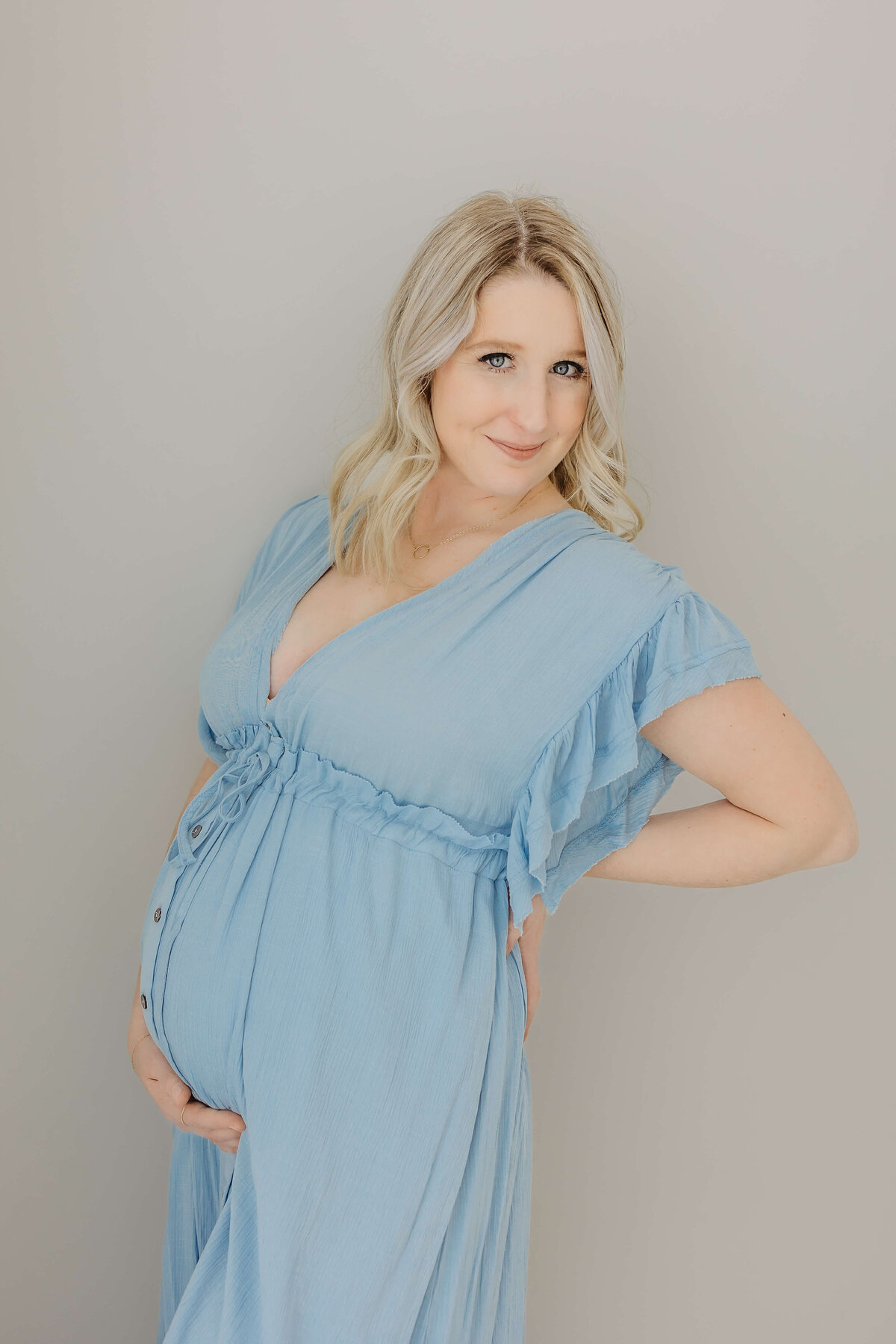 Pregnant mom in blue dress standing up and smiling at camera
