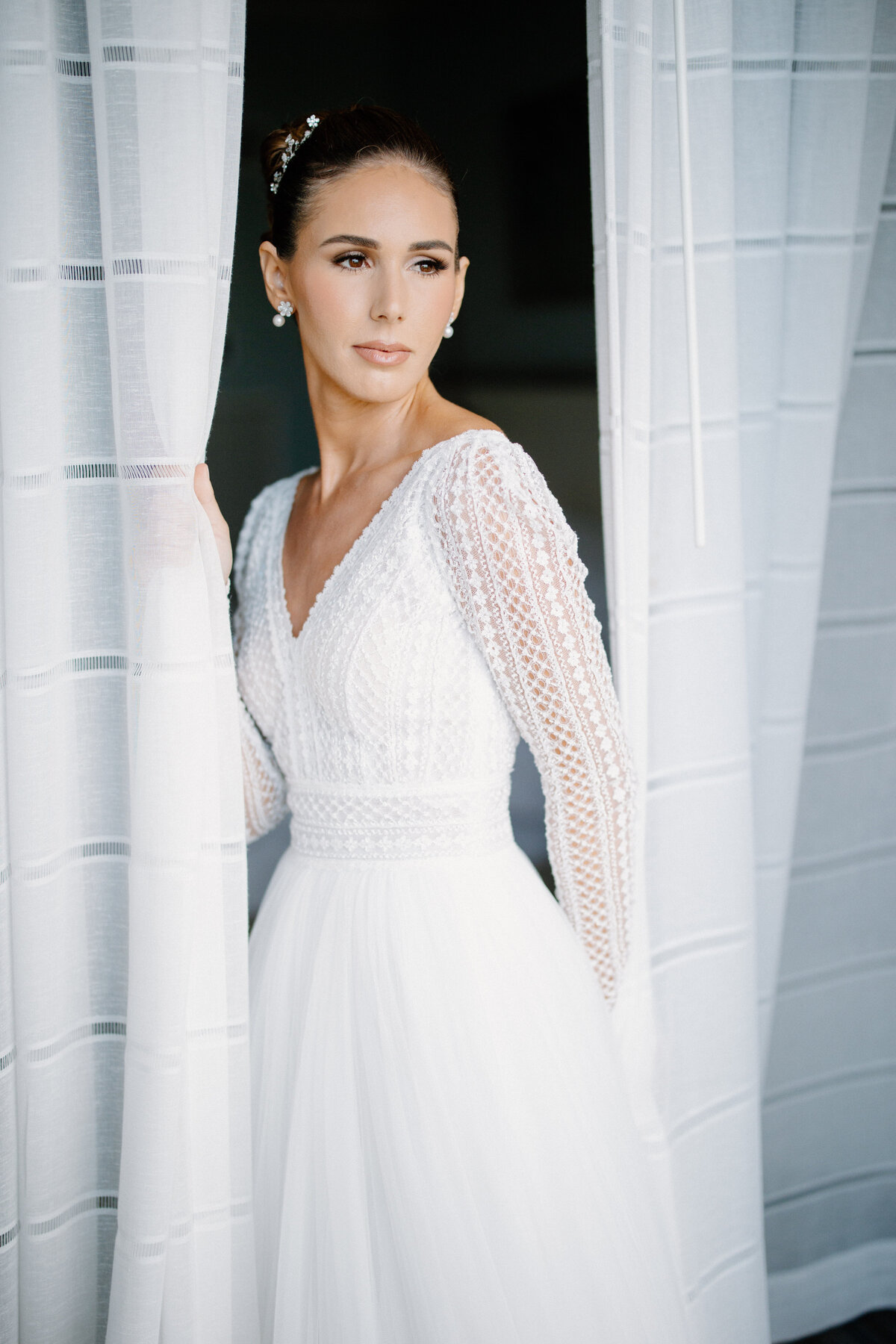 Bride in a lace long-sleeved dress gazing out a window, photographed by Rodrigo Varela Photography.