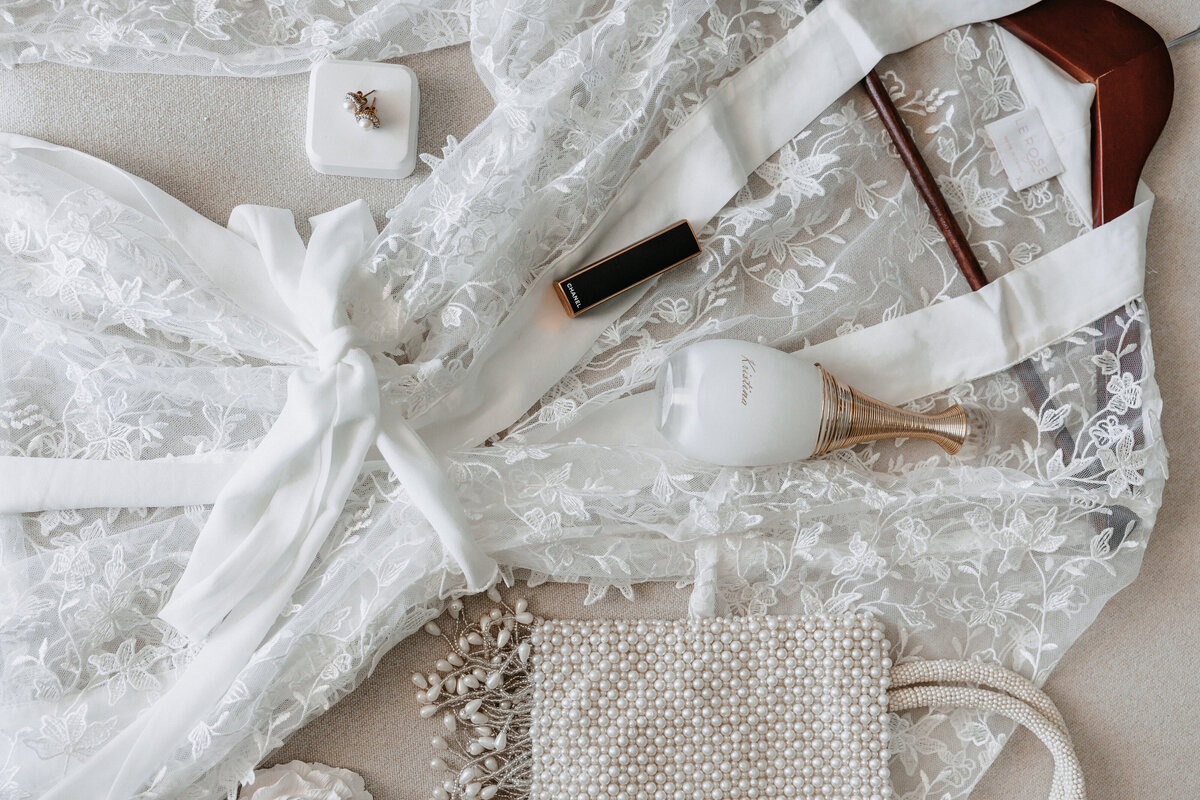 flat lay detail photo of wedding ring, lipstick, perfume, purse and robe