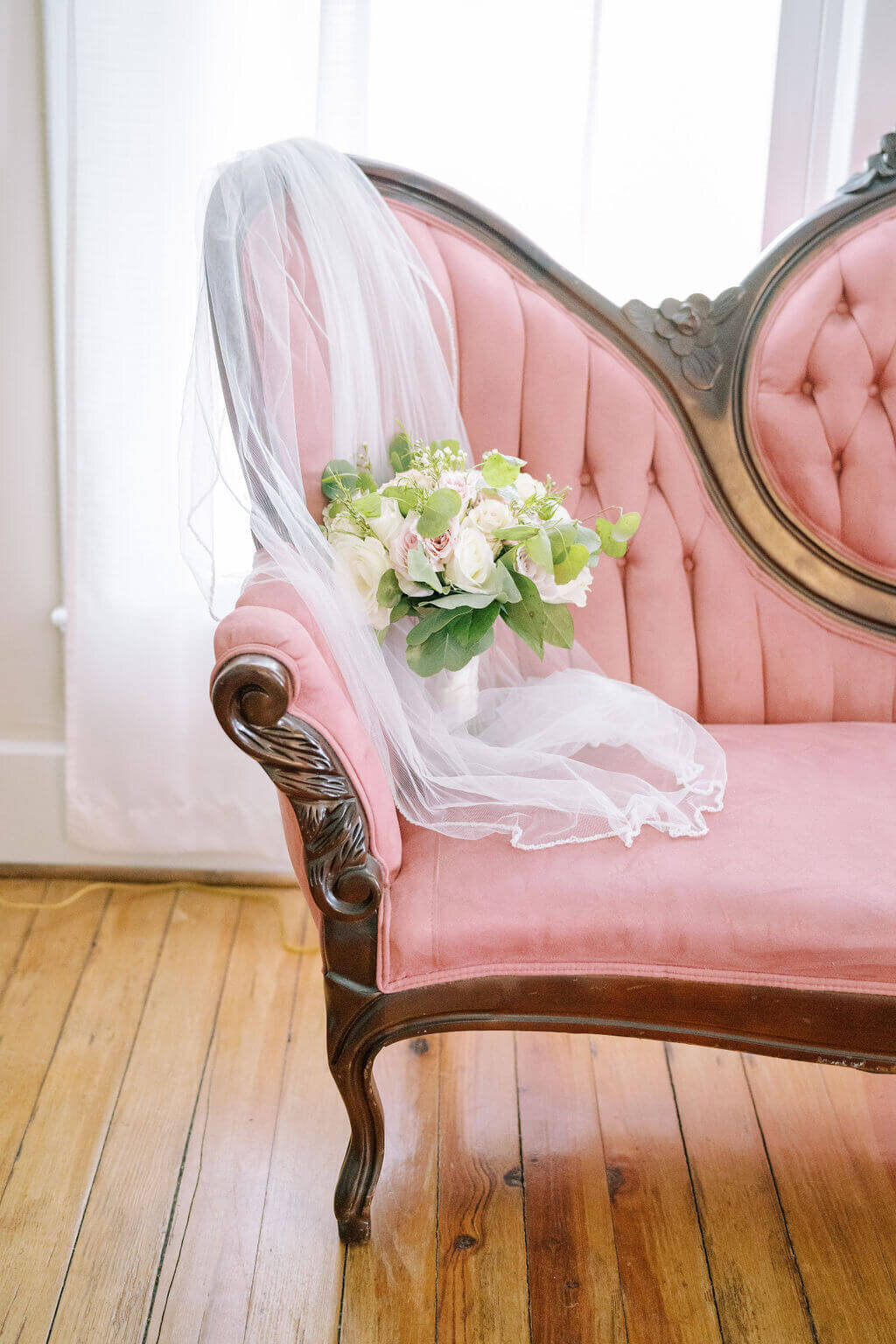 Flower bouquet sitting on pink couch with veil